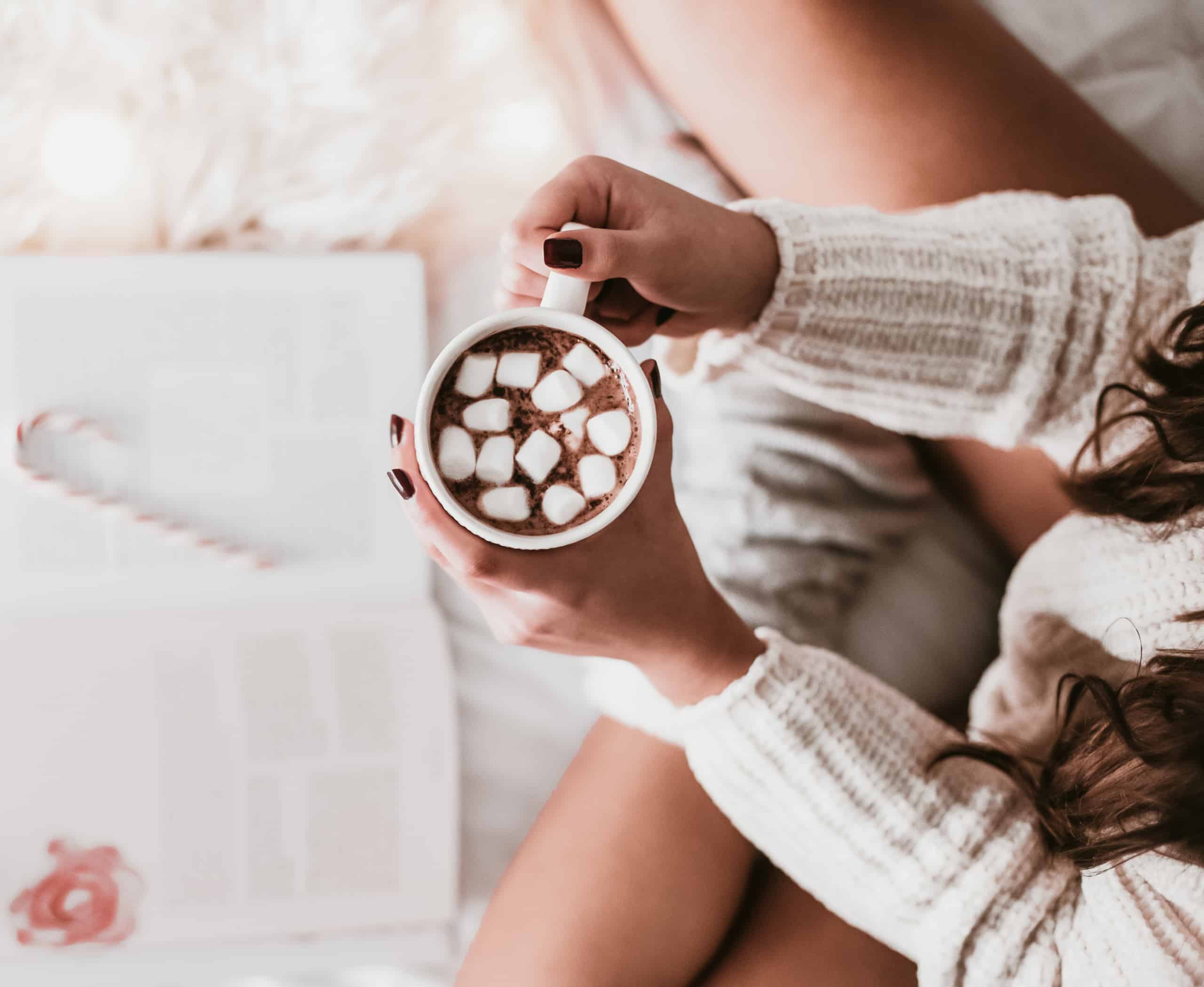 overhead view of a non descript woman in a cozy sweater holding a cup of hot coco with marshmellows