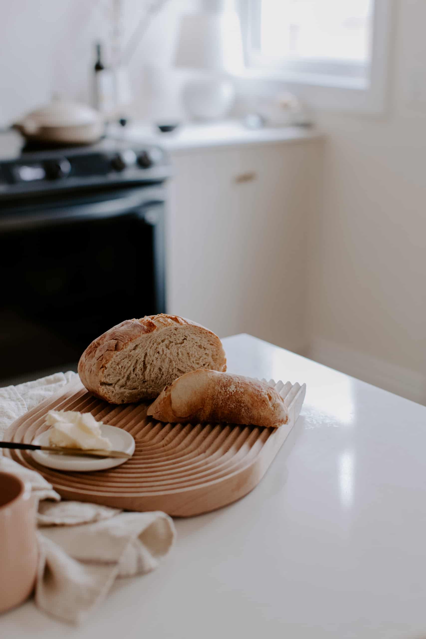 sliced loaf of bread and butter on a wooden cutting board with a kitchen scene in the background