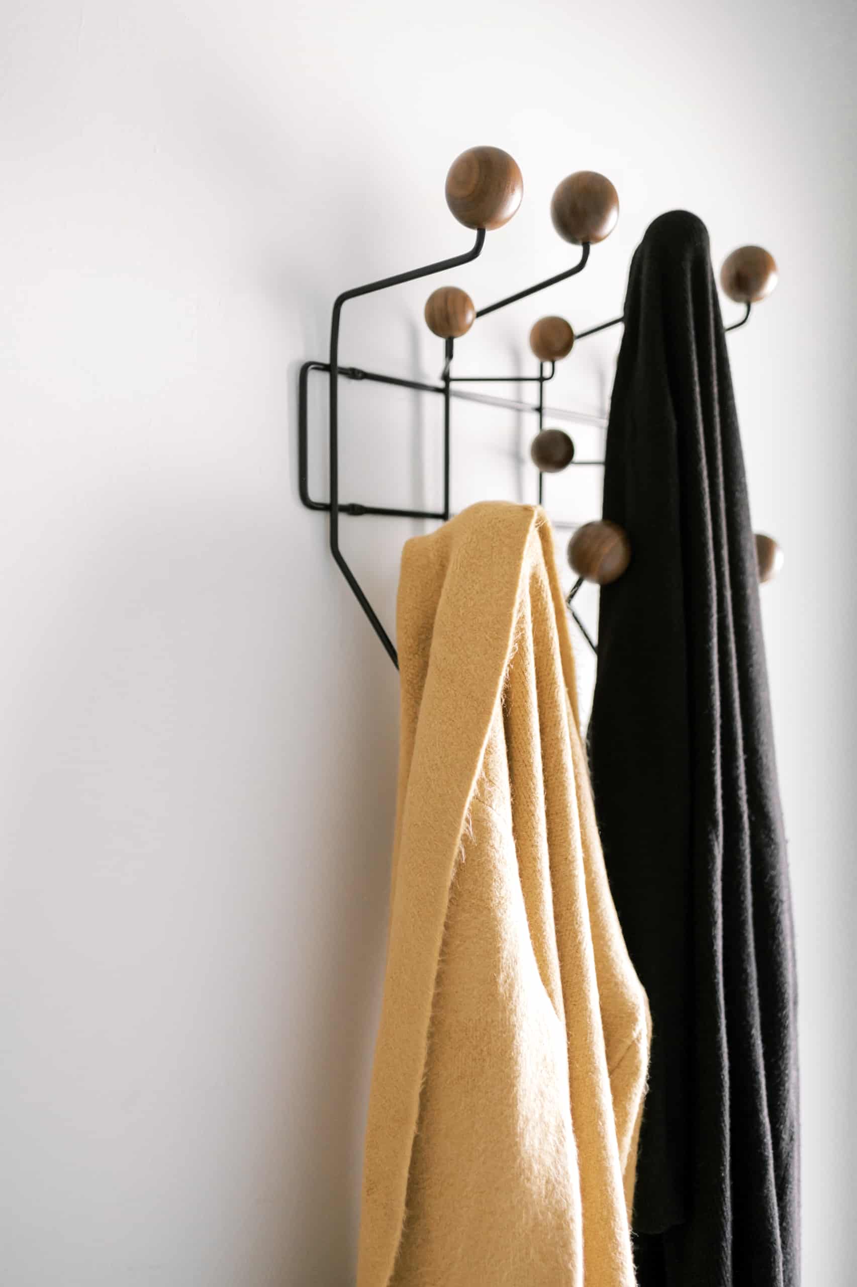 two sweaters hanging on a wall mounted coat rack