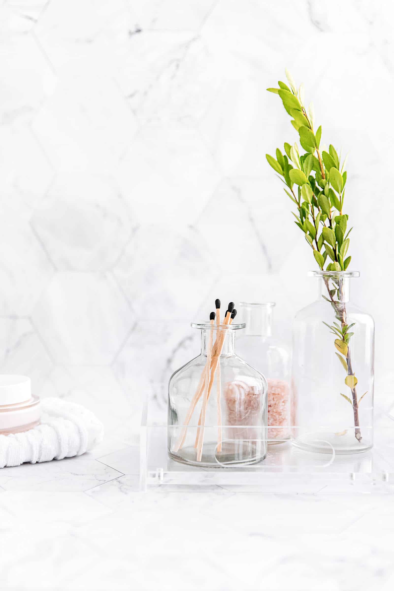 Bathroom counter with small vessels of procuts and a branch of leaves