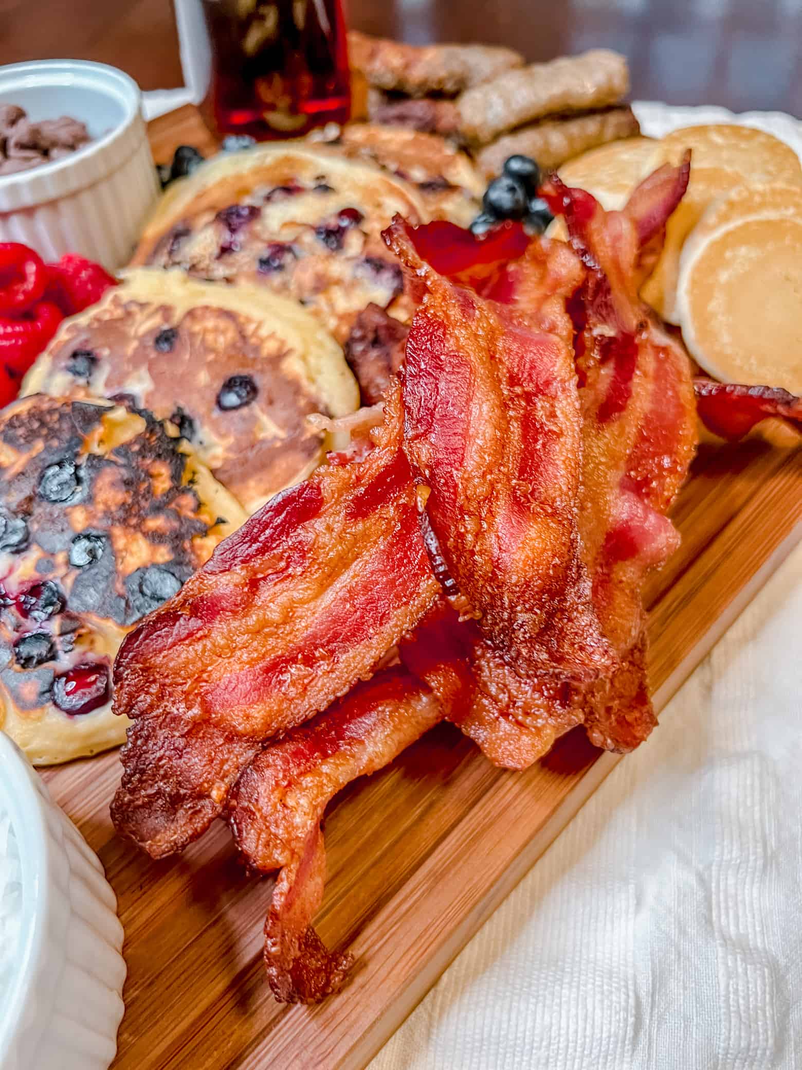 a pile of bacon along with blueberry pancakes and other breakfast foods on a charcuterie board