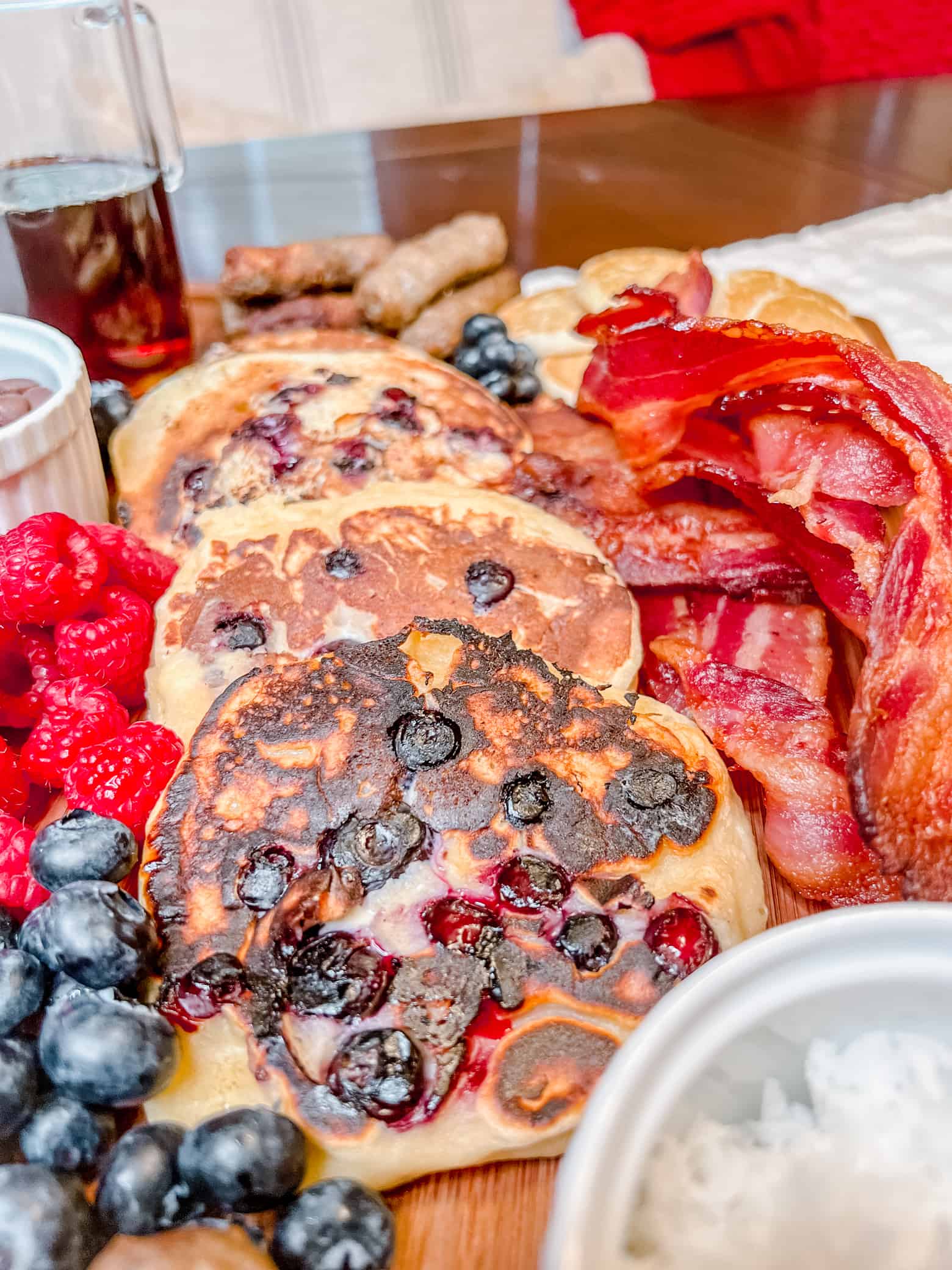 close up of a charcuterie board of breakfast items including pancakes, sausage. bacon, berries, and chocolate chips