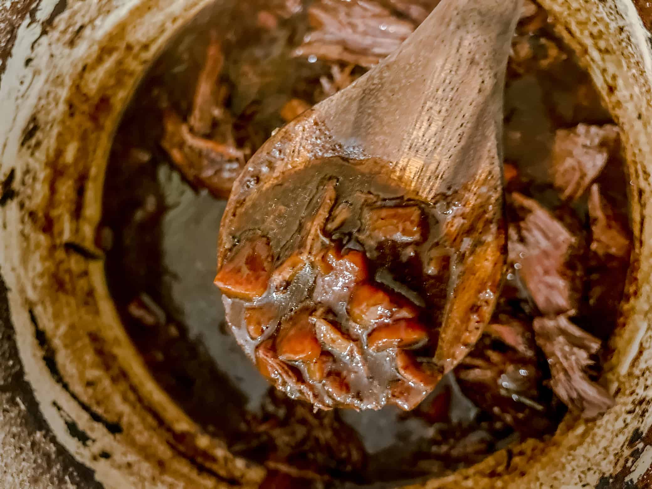 wooden spoon over a pot of shreeded beef with carrots