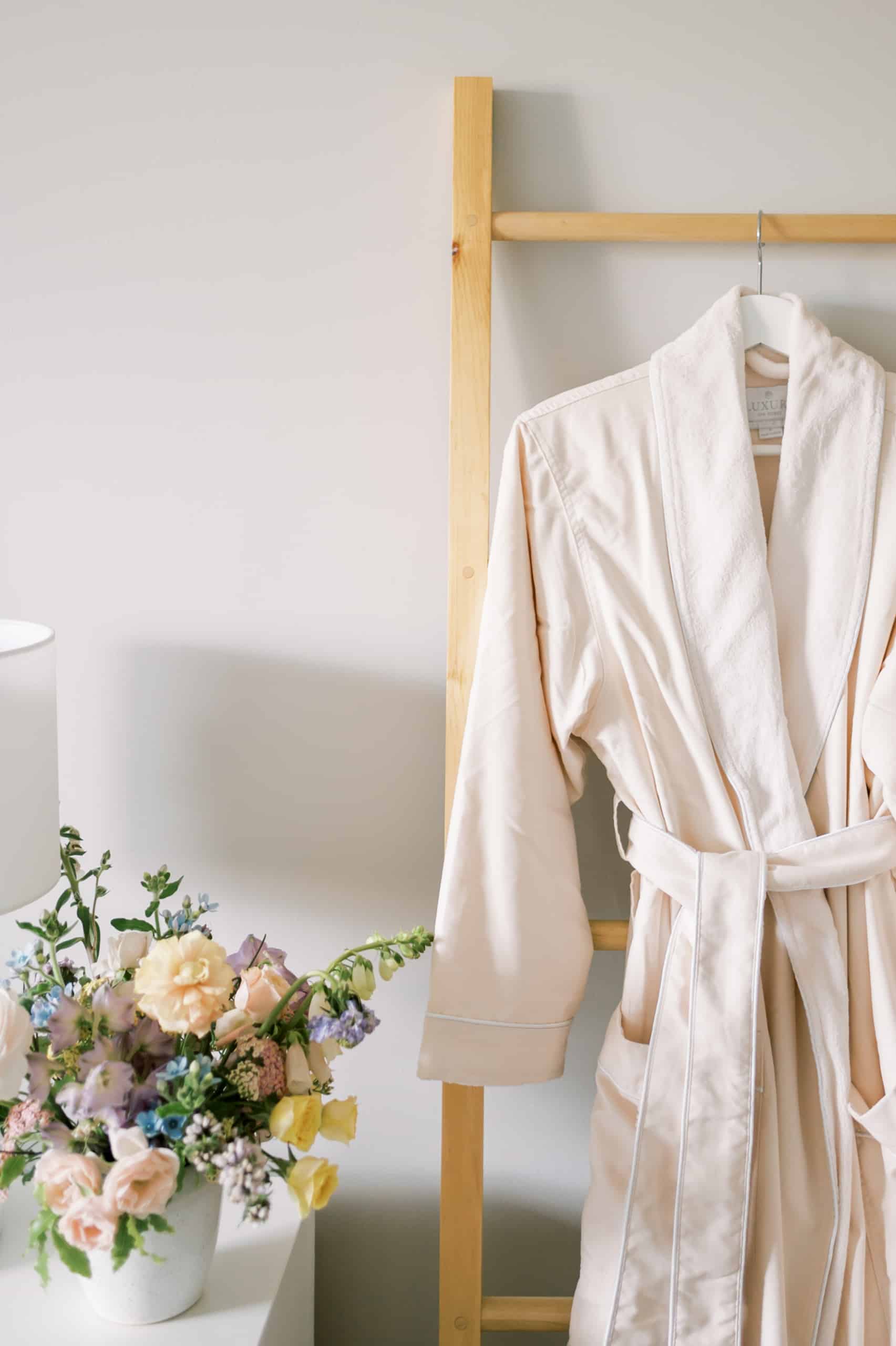 cozy spa robe hanging on decorative ladder next to dresser with floral arrangement on top