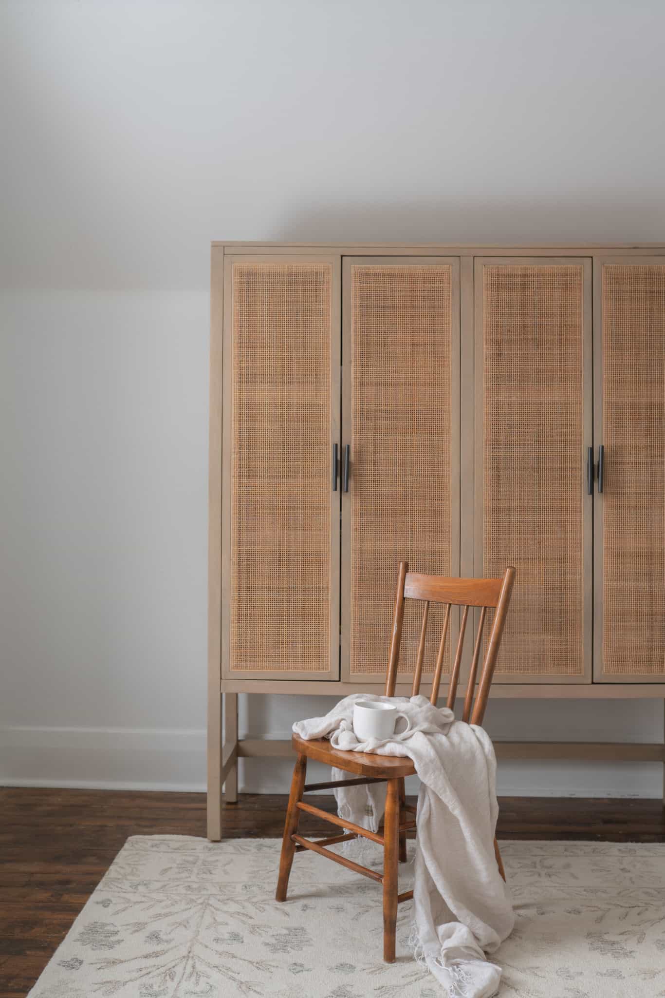 bedroom dressor with small wooden chair with linen draped over it and a coffee mug in the seat