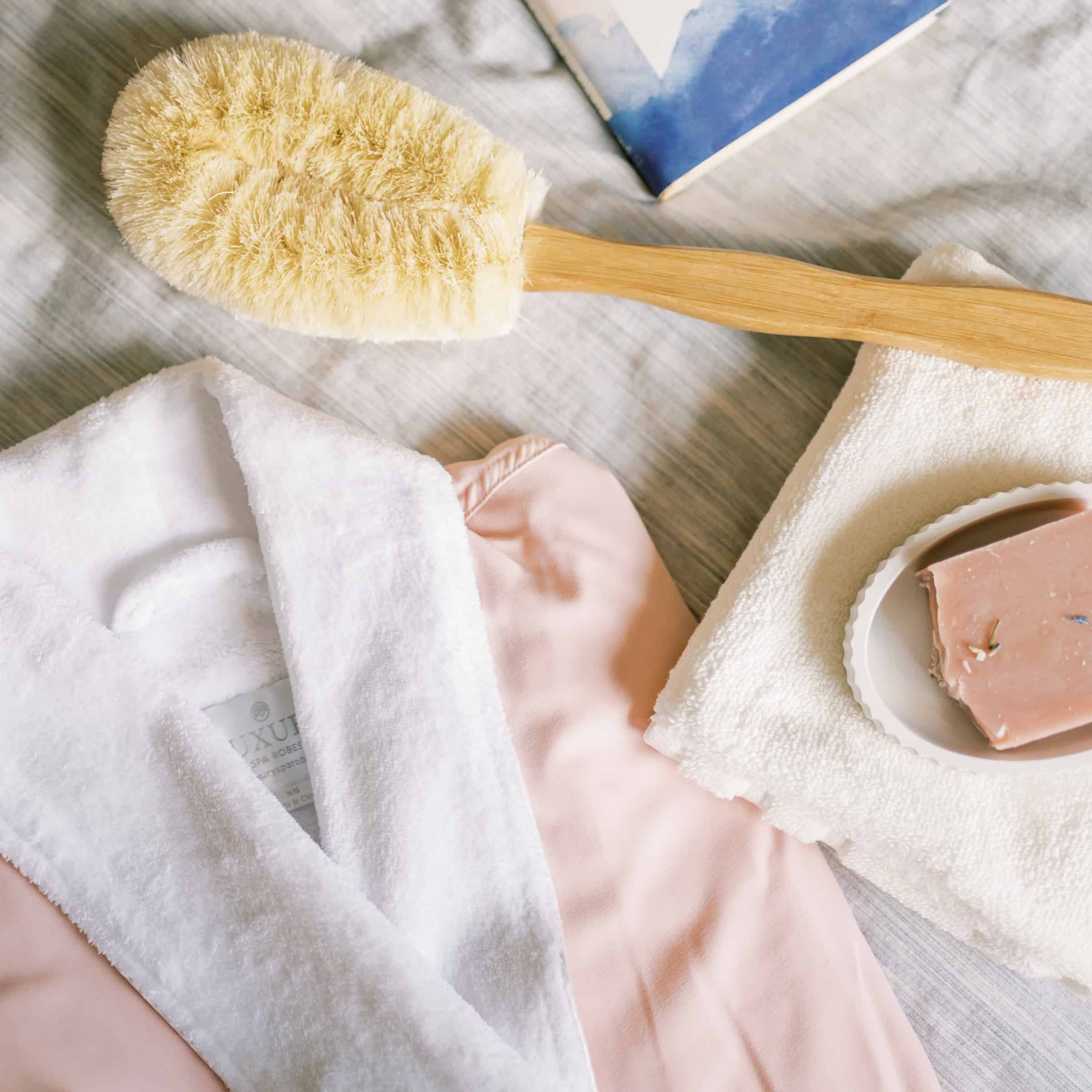 overhead view of a bathrobe, body brush, bar of soap, and washcloth laid out on a cloth cover