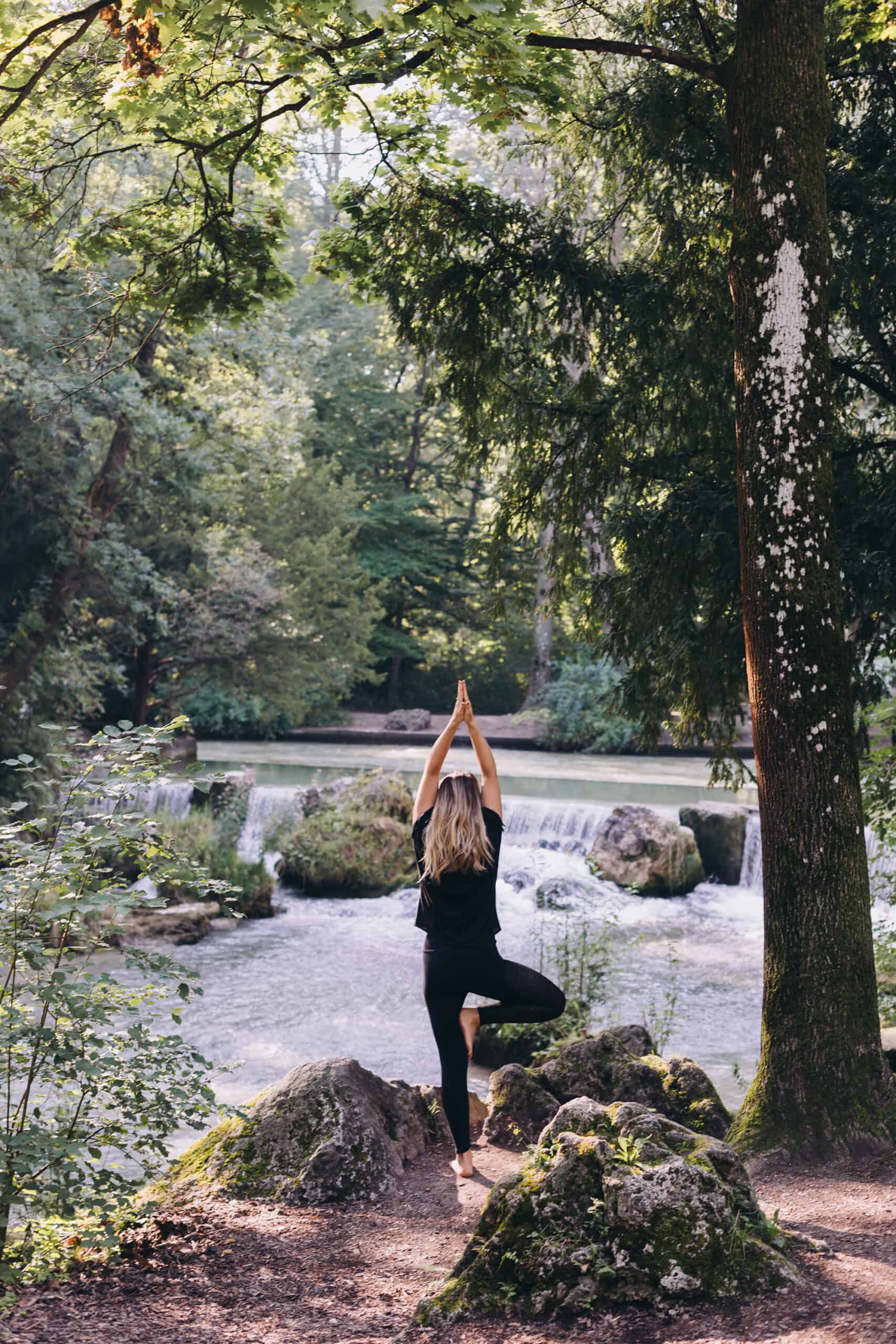 non-descript woman practicing yoga in a lush green park near a stream