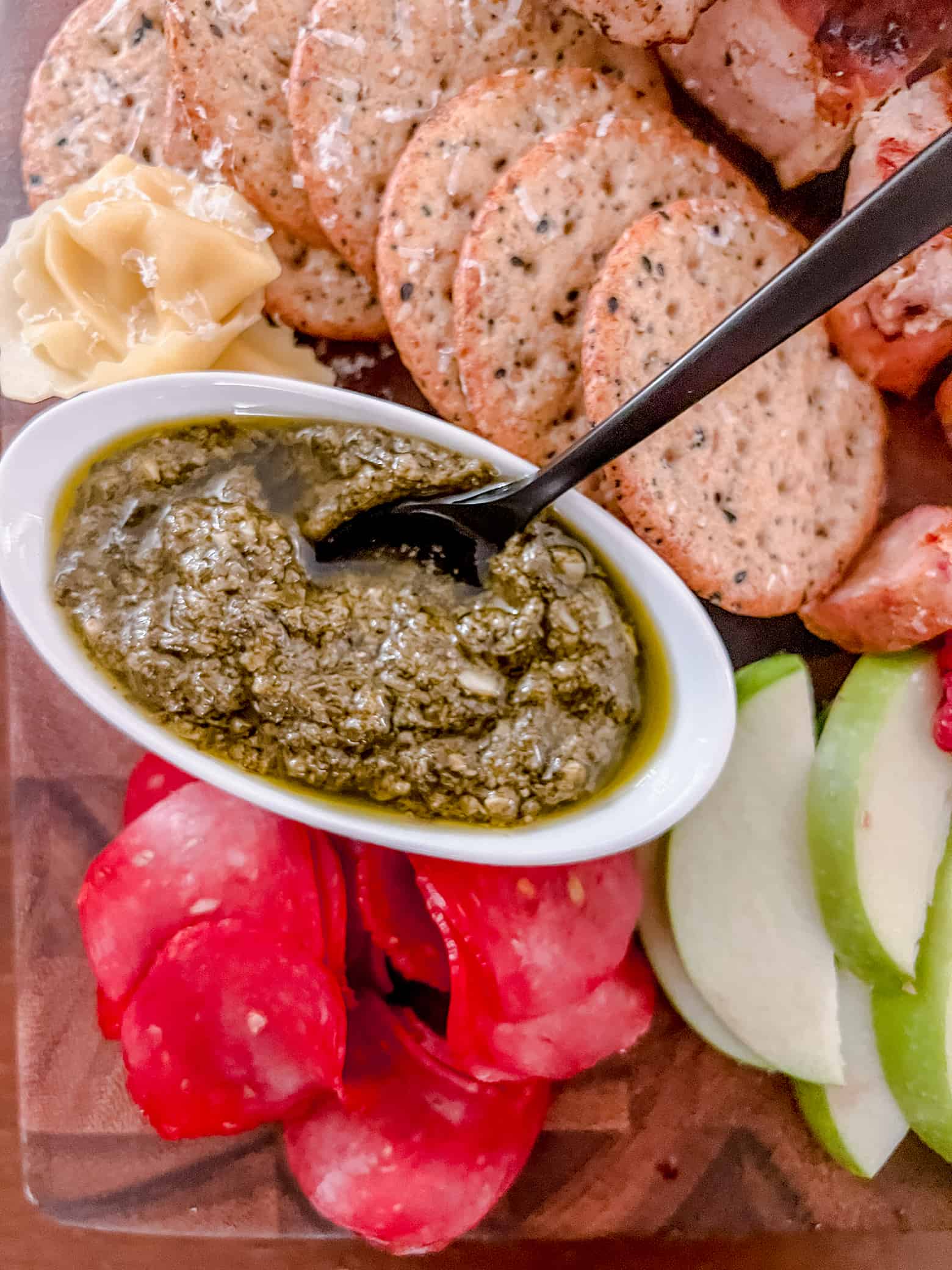 Extreme close up of a charcuterie board with a bowl of pesto with a spoon in it and various food items