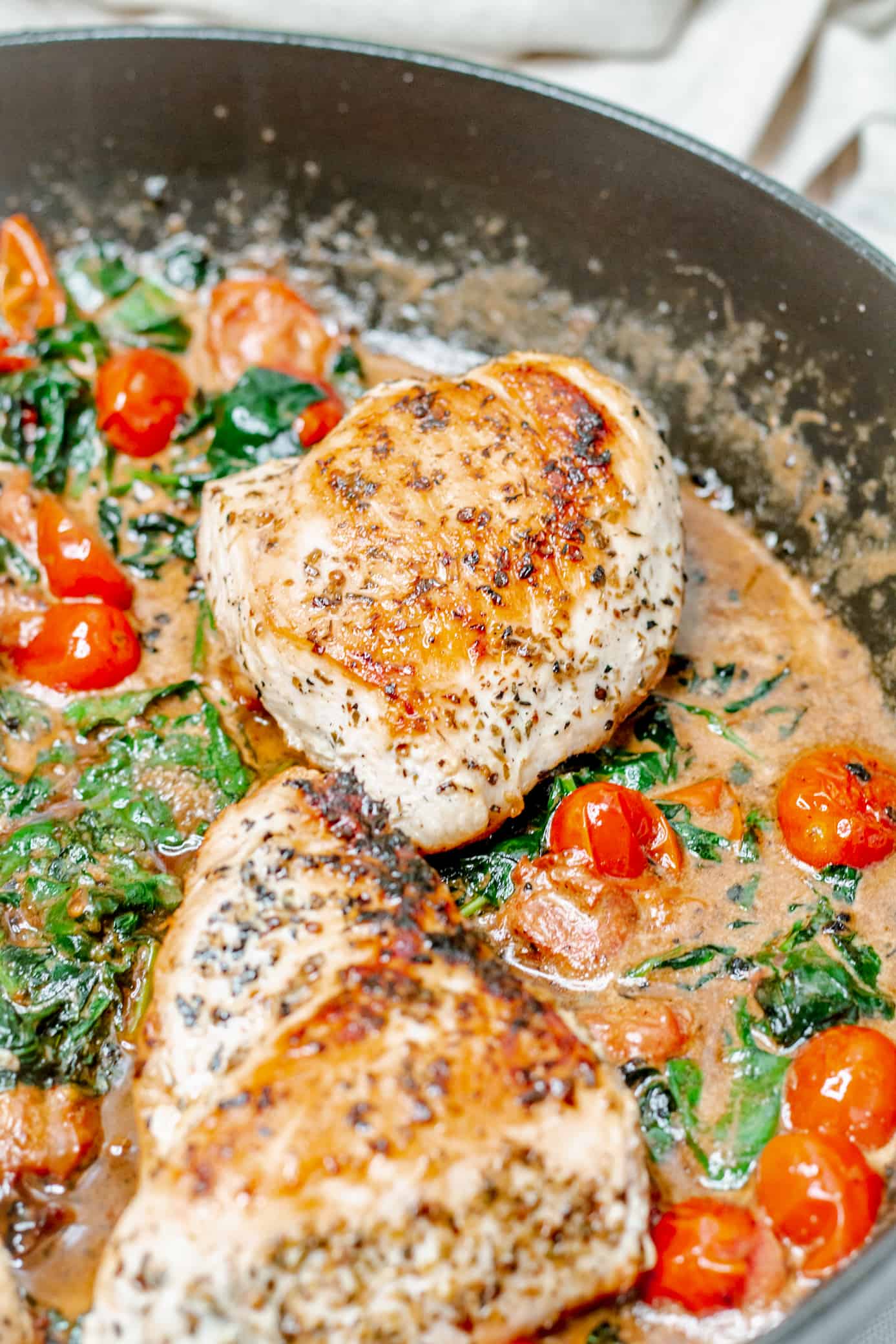 Overhead view of a pan filled with creamy tuscan chicken, wilted spinach, and grape tomatoes