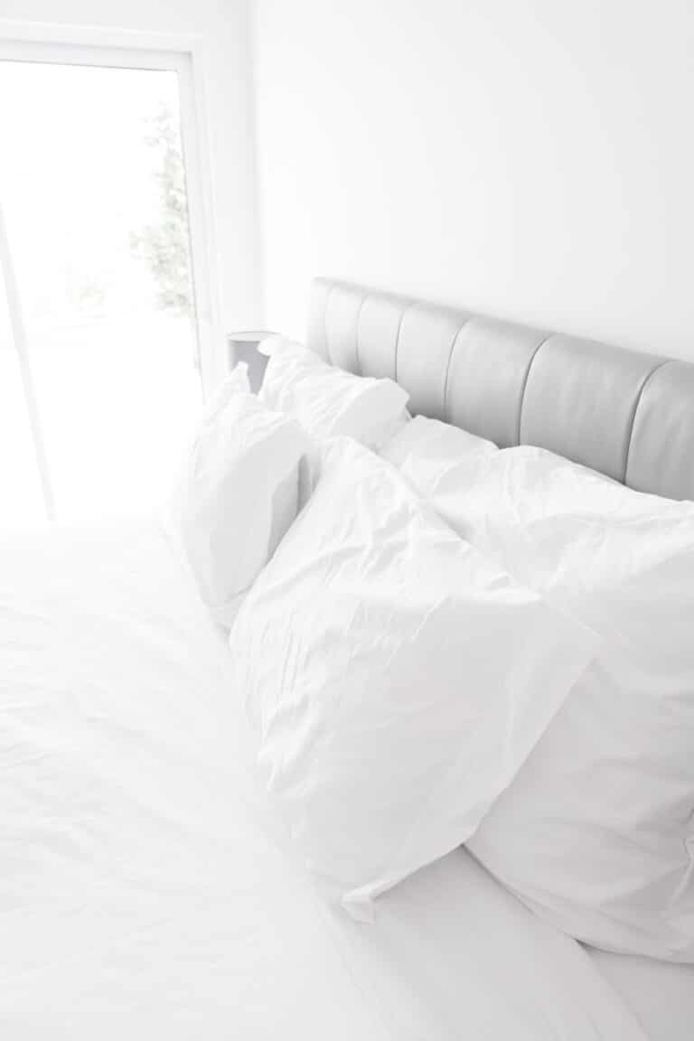 Head of a made bed with pillows near an open window