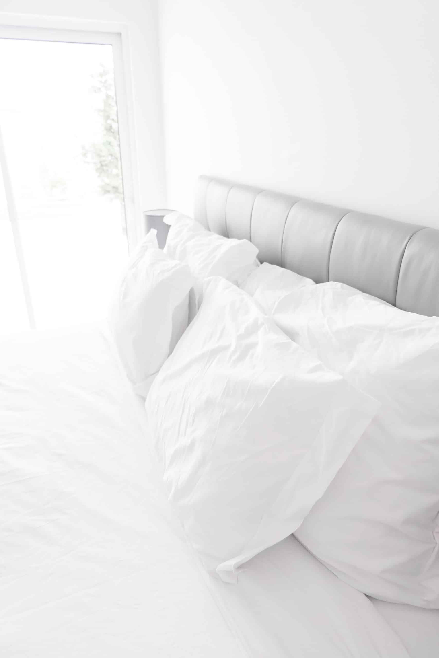 Head of a made bed with pillows near an open window