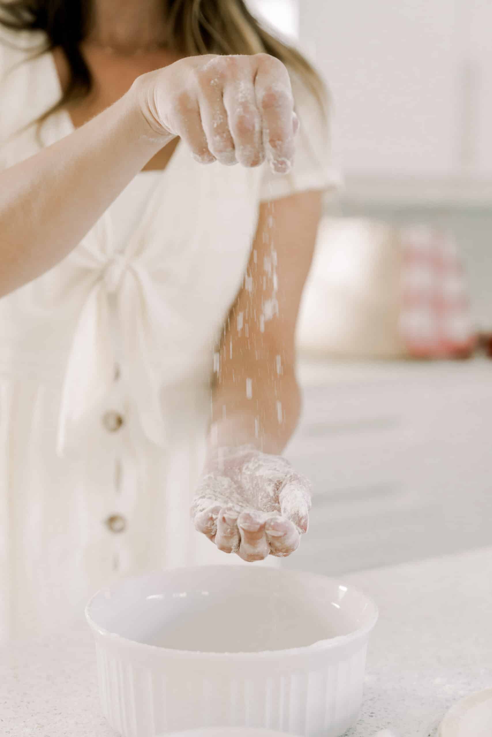 Non descript woman using her hands to drop flour into a ceramic bowl