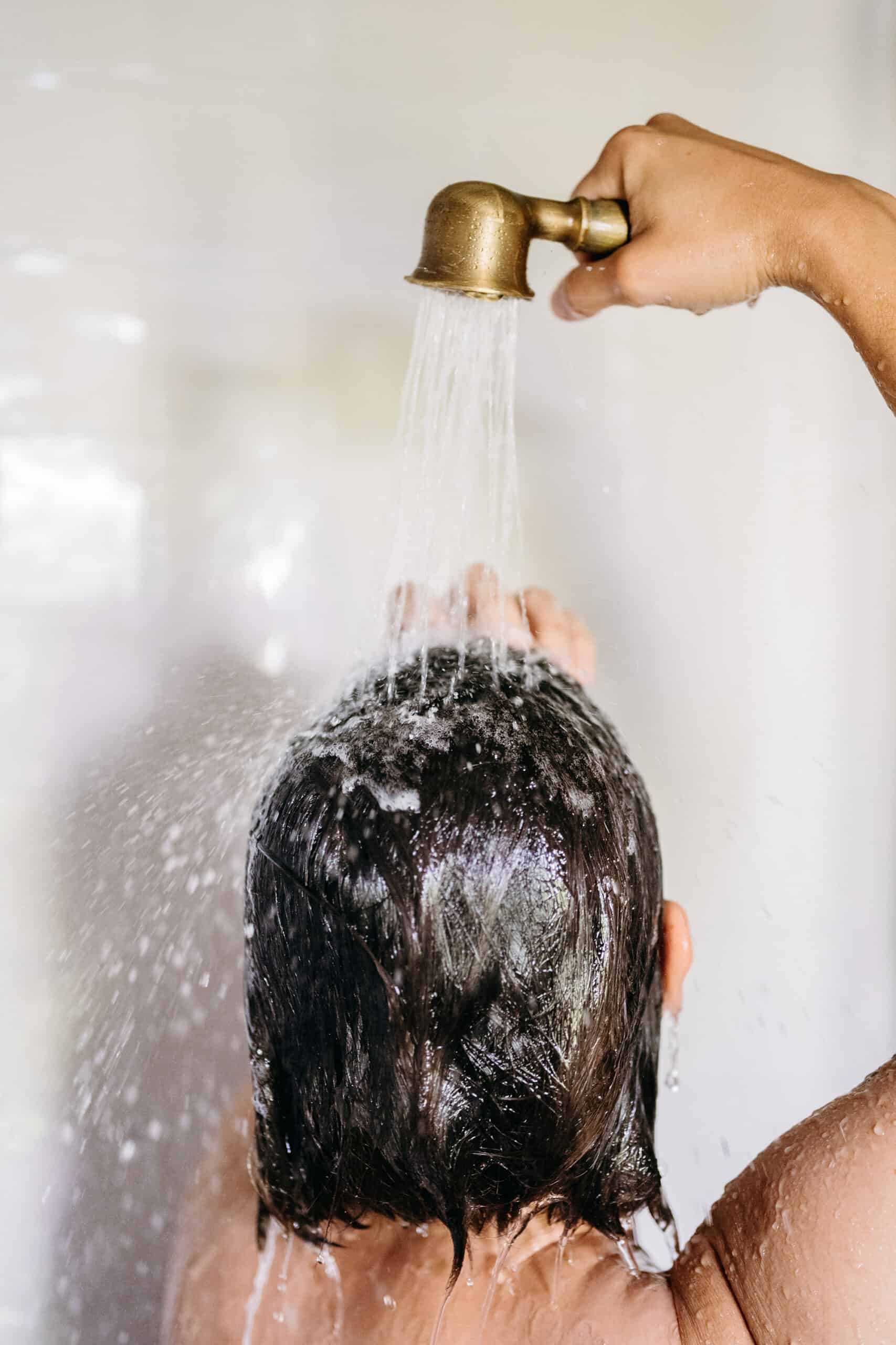 a non descript woman holding a showerhead over her head, washing hair