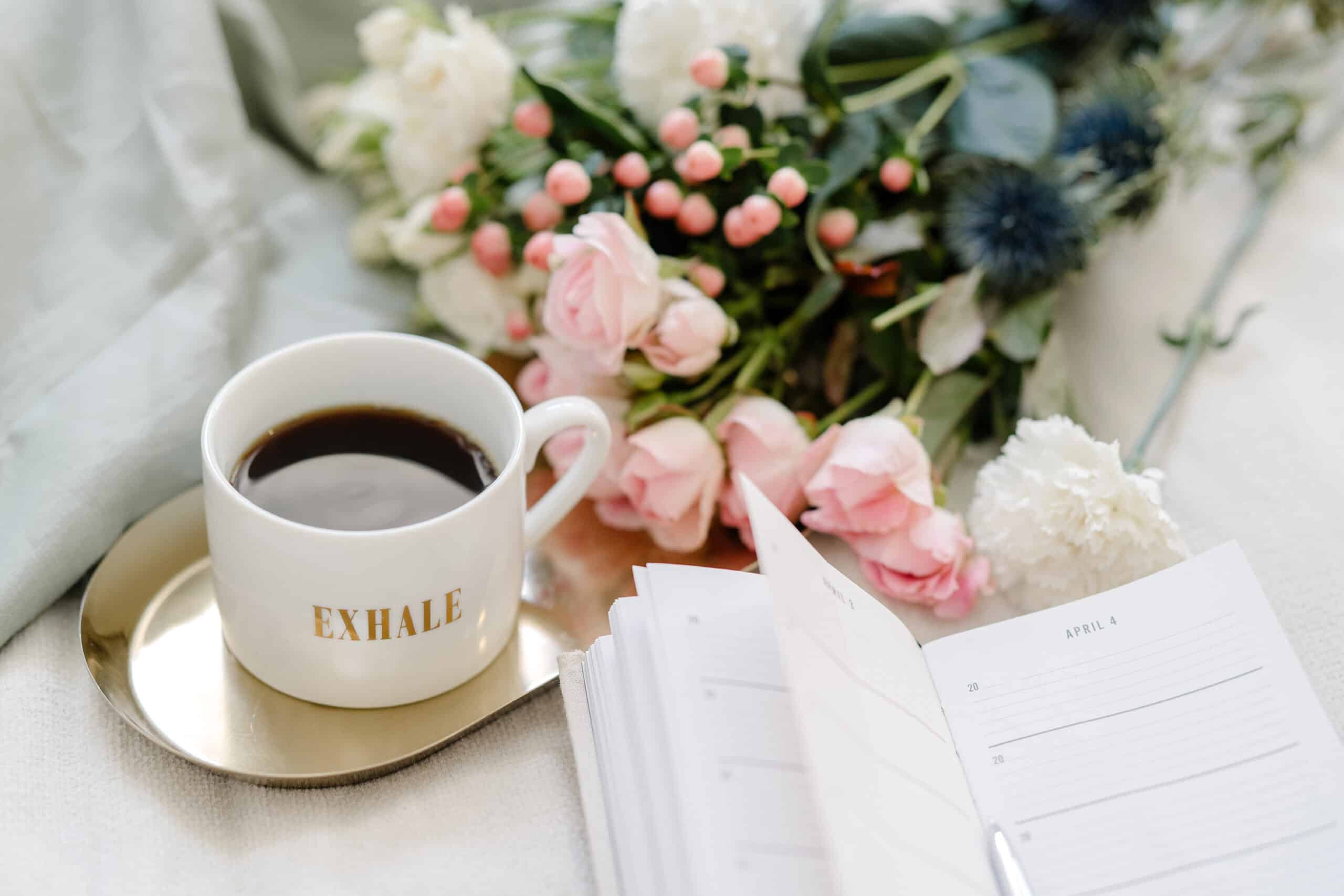 overhead view of cup of coffee on a metal tray along ith a bouquet of flowers and an open date book