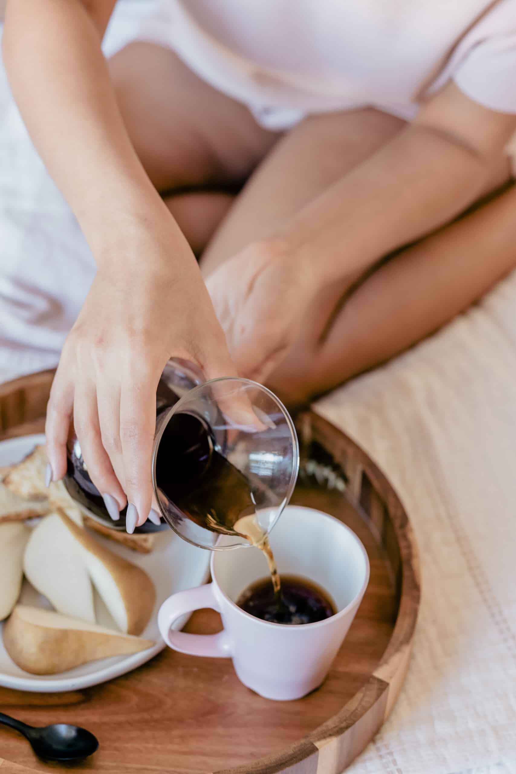 non descript woman pouring coffee from a chemex into a mug. The mug is on a tray with a plate of sliced pears