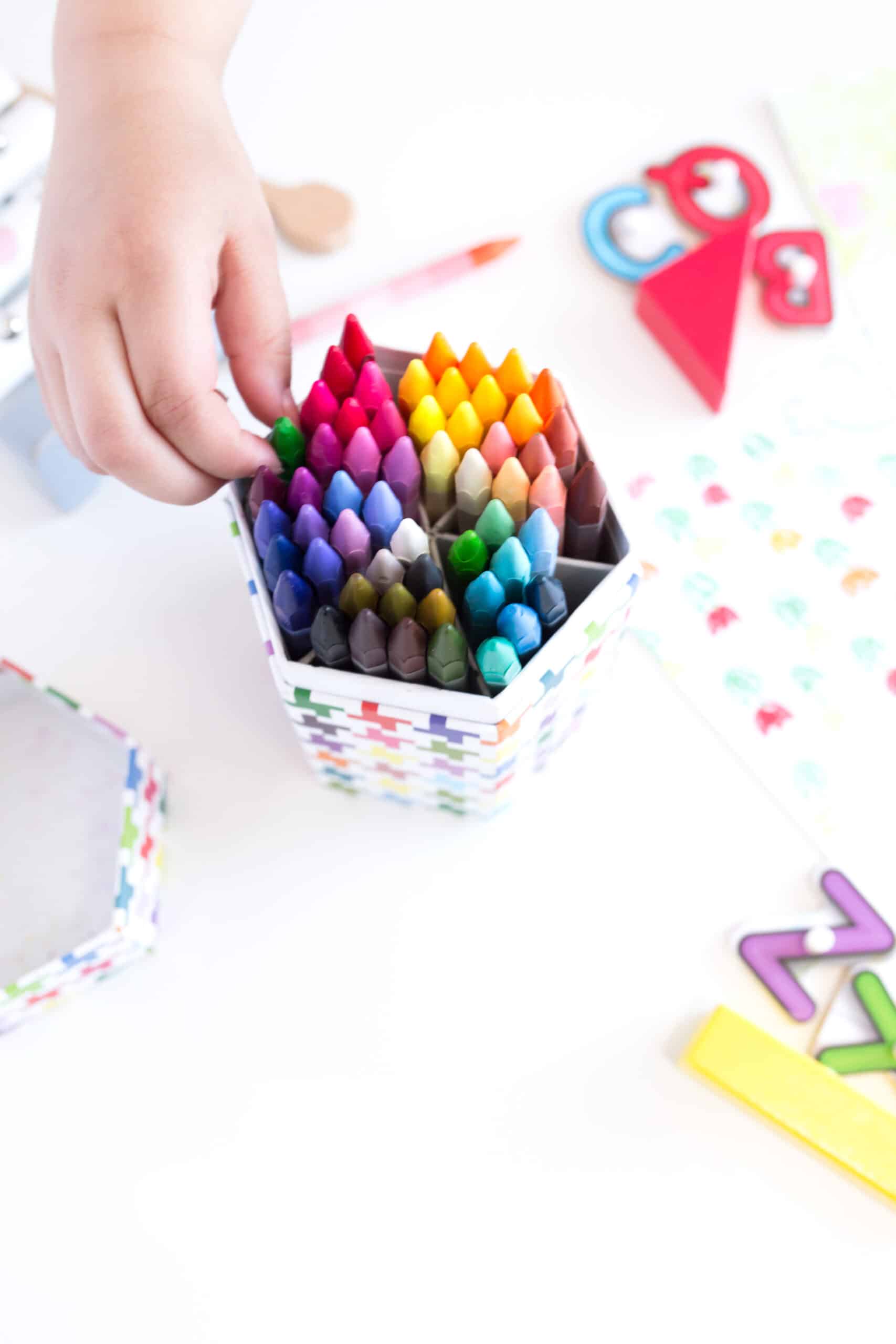 non descript child's hand reaching for a crayon in a bin. Several crafts also on the table