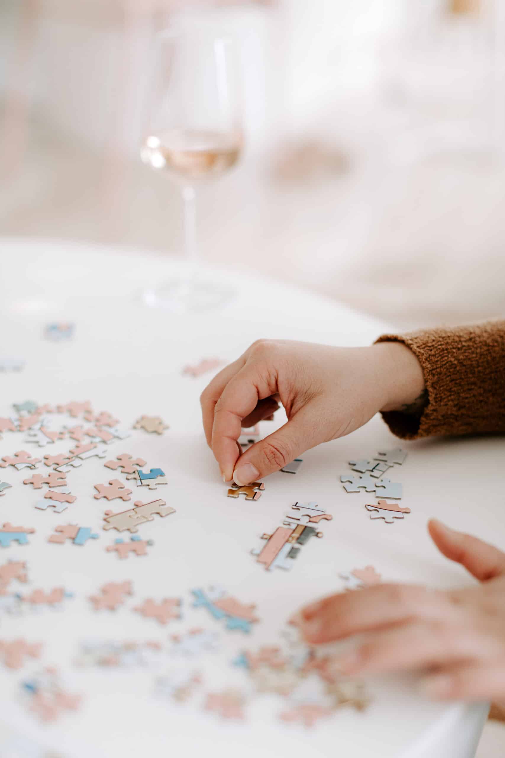 non-descript hands putting a puzzle together with a wine glass in the background