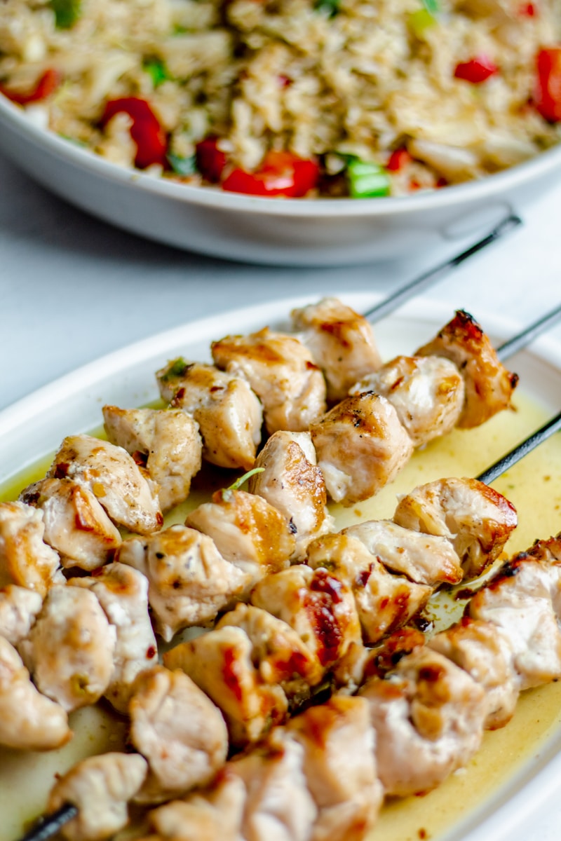 chicken kabobs in a butter sauce with a rice dish in the background