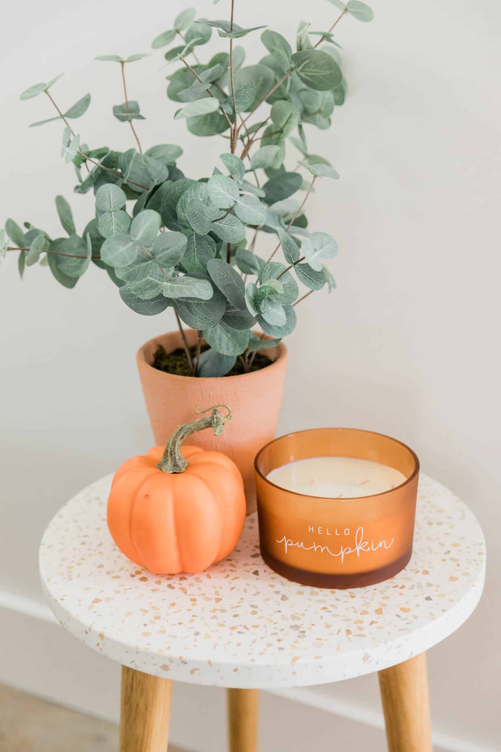 small side table with a faux plant, small pumpkin, and candle