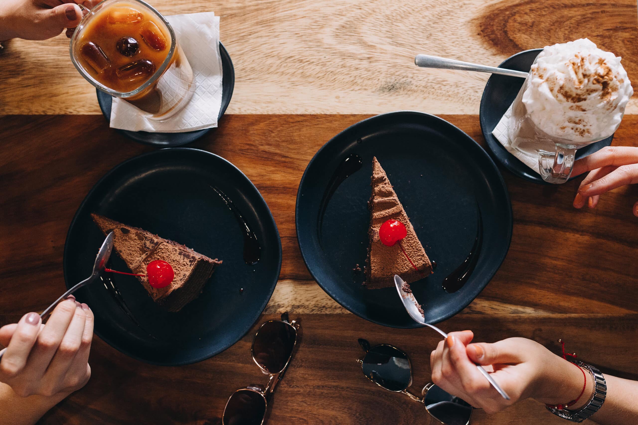 Overhead view of two people about to eat slices of chocolate cake and drink dessert type drinks (cocoa and cider).