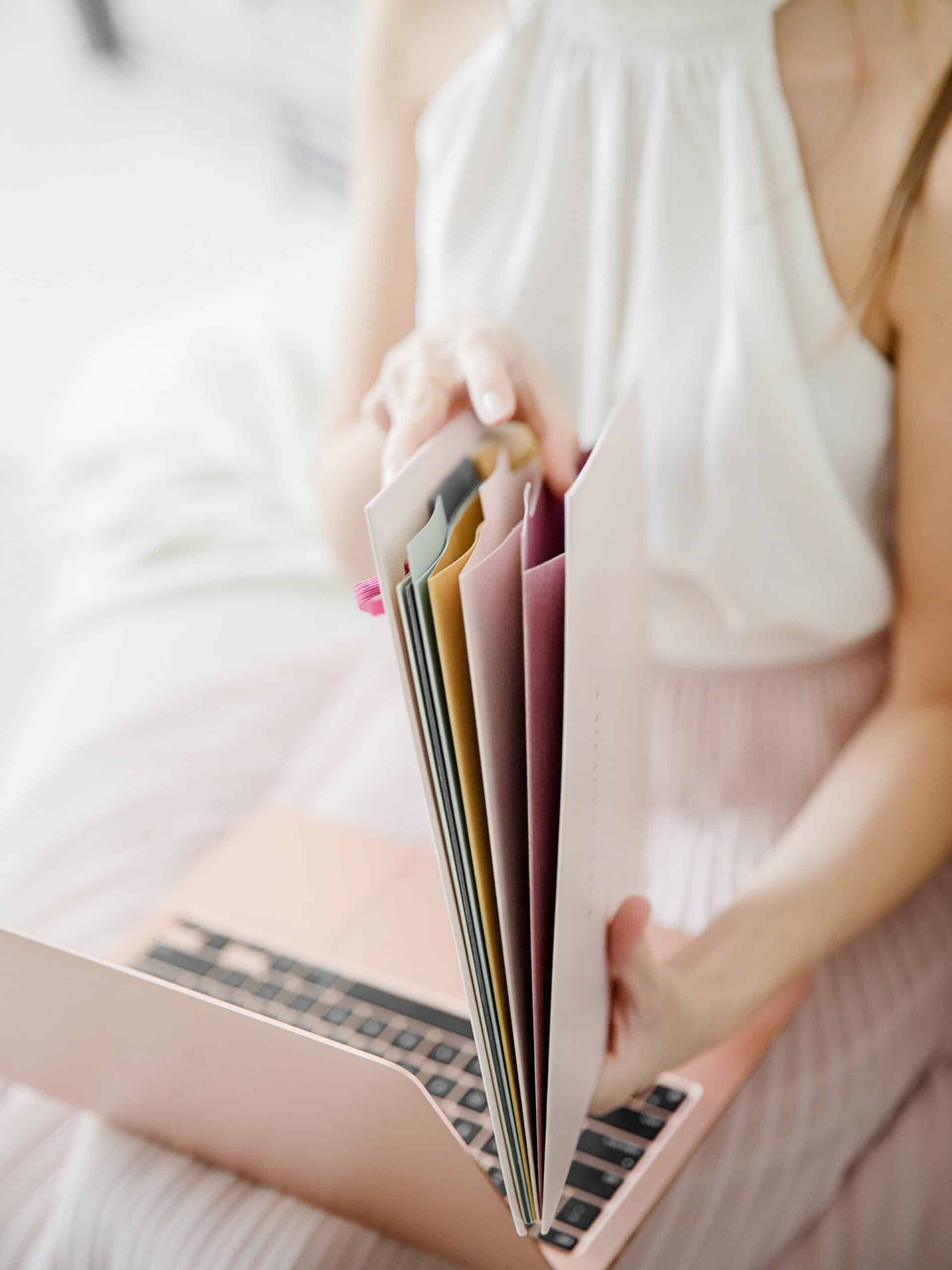 A woman holds a file folder in her hands and a laptop on her lap as she looks through the file folder.