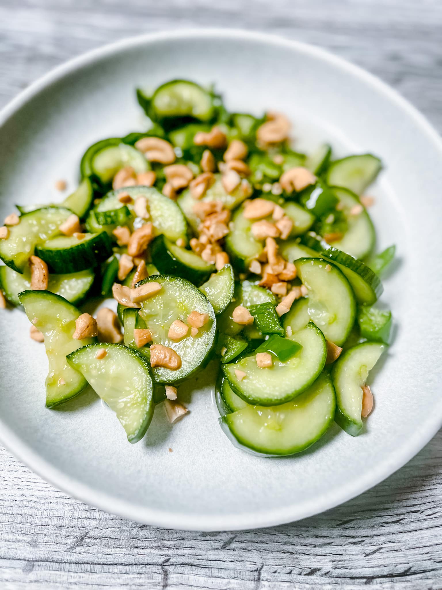 Sliced, halved cucumbers with dressing, jalapeno pepper slices, and chopped cashews in a shallow bowl.