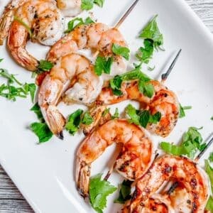 Grilled shrimp skewers surrounded by a sprinkling of parsley lie on a white plate.