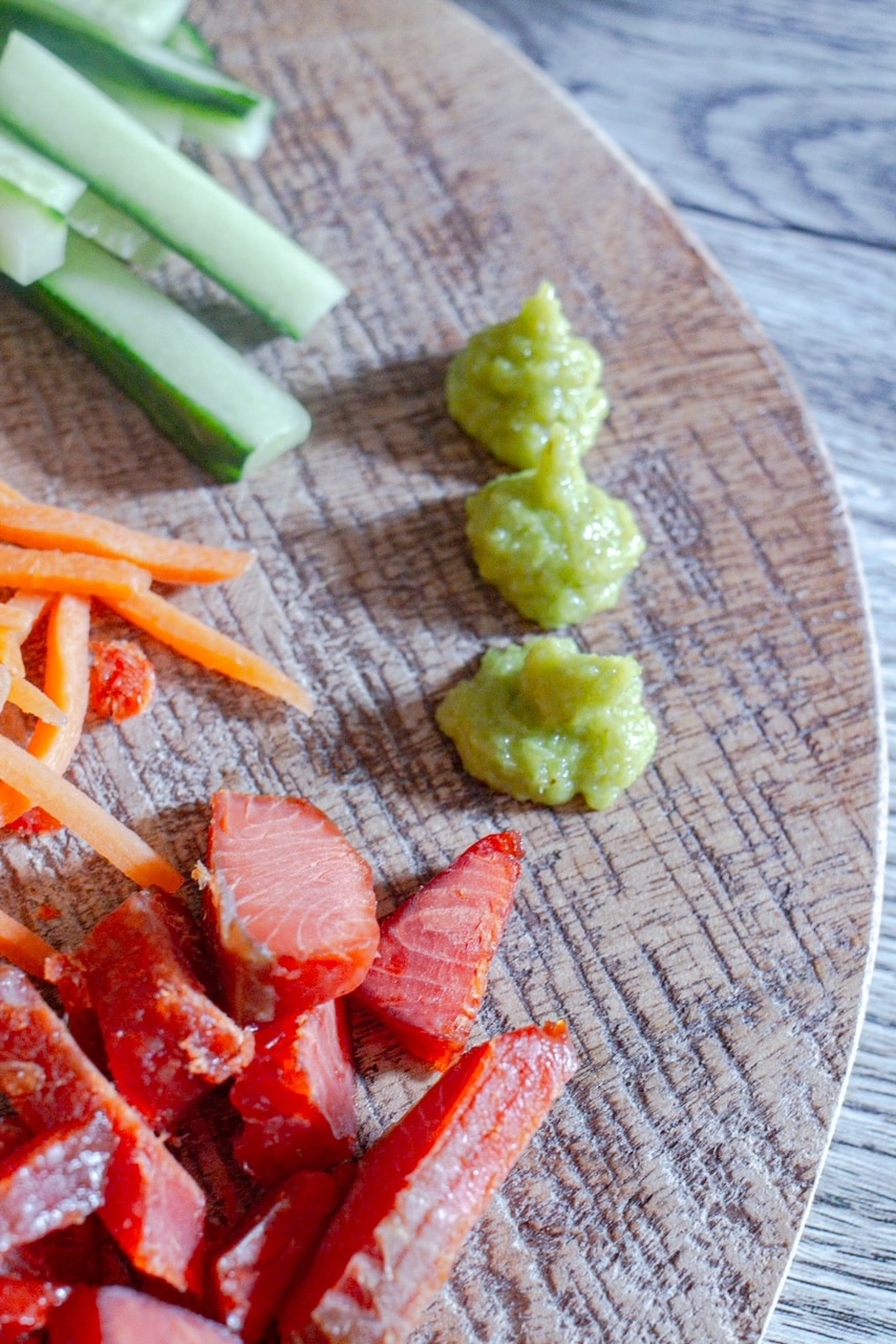 extreme closeup of smoked salmon roll board, focusing in on wasabi, salmon, carrot sticks, and cucumber sticks