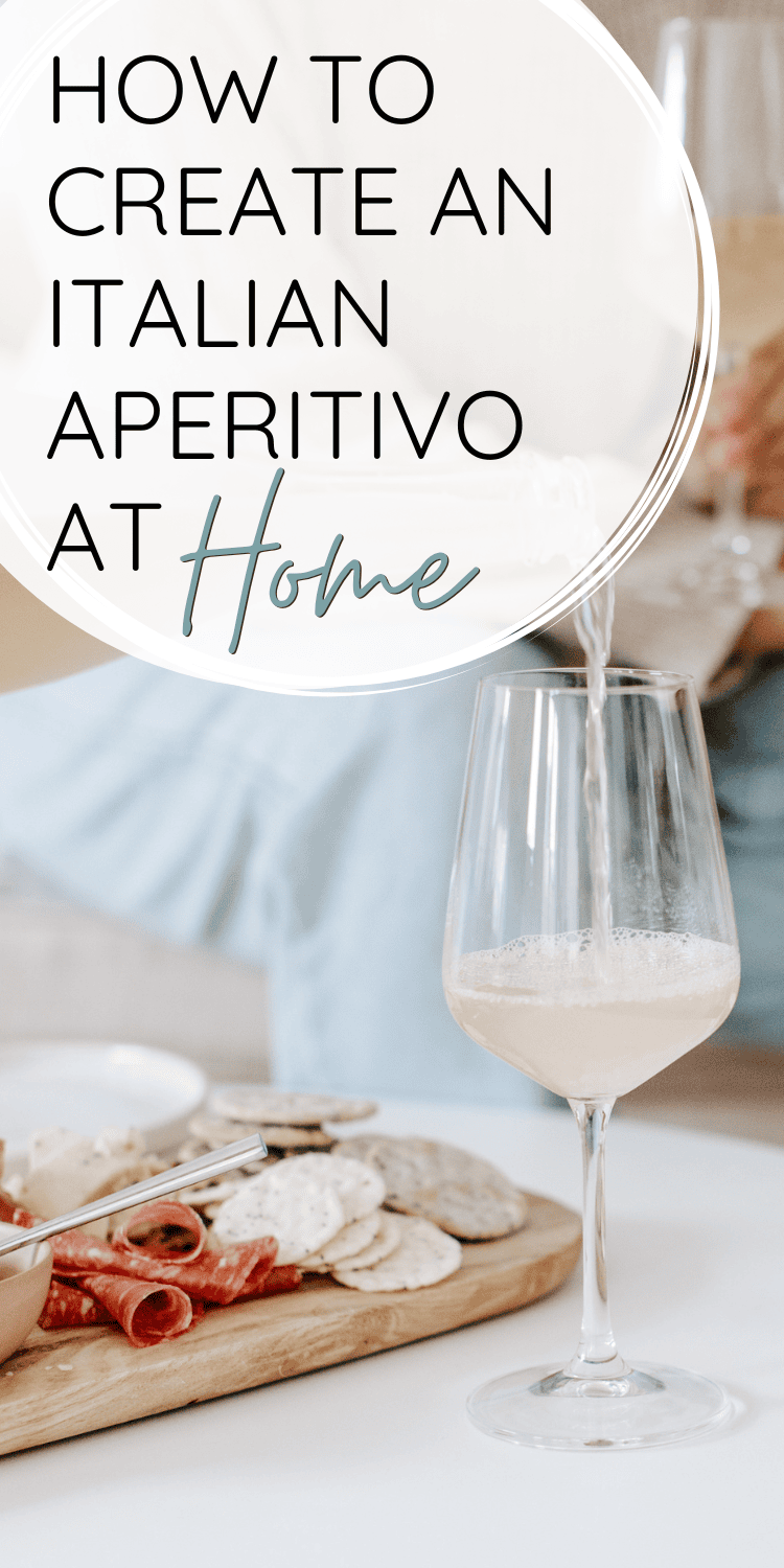 A chic Italian aperitivo setup with a wooden board of cured meats, crackers, and cheese paired with a glass of white wine being poured. The text overlay reads "How to Create an Italian Aperitivo at Home.