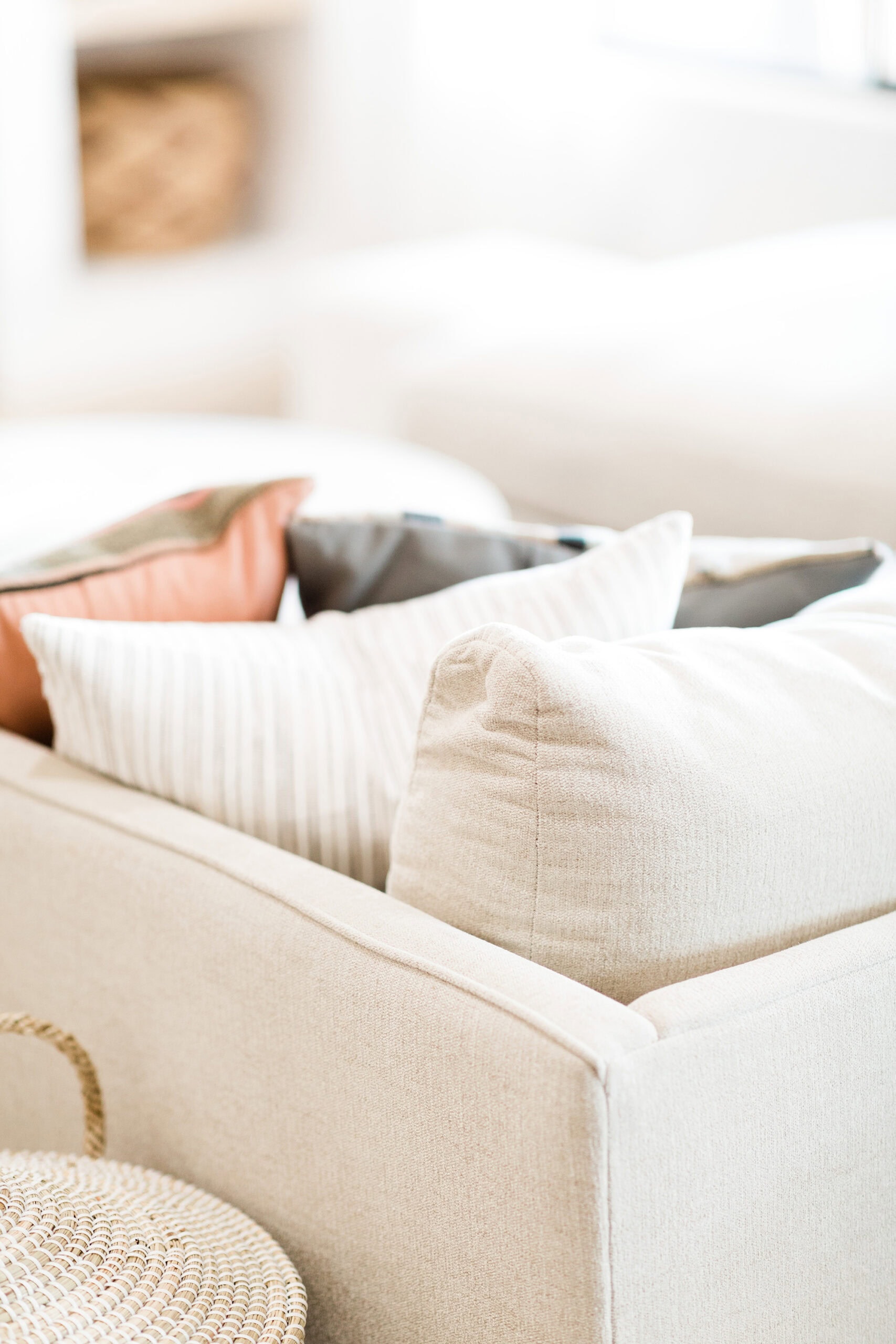 A soft, neutral-toned sofa adorned with striped and solid throw pillows, complemented by a nearby woven basket, adding a touch of texture and coziness to the room.