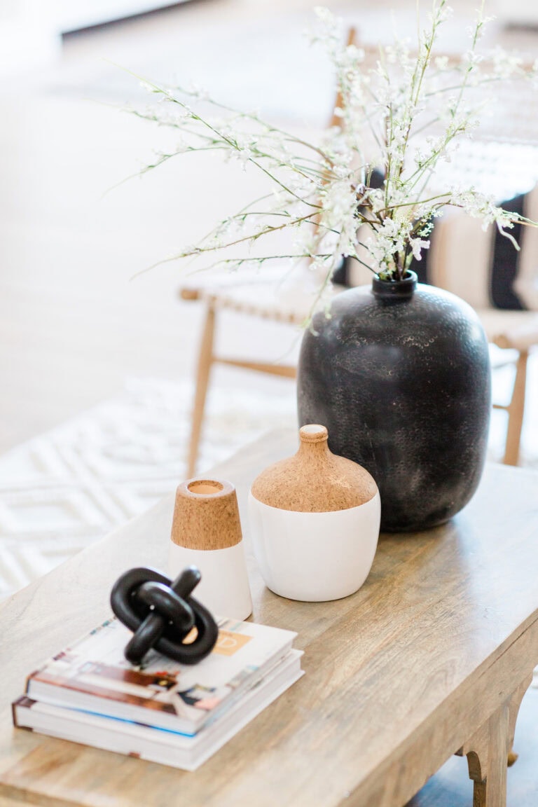 A beautifully styled coffee table featuring a large black vase with delicate white flowers, paired with decorative white and cork containers and stacked books for a sophisticated yet homey look.