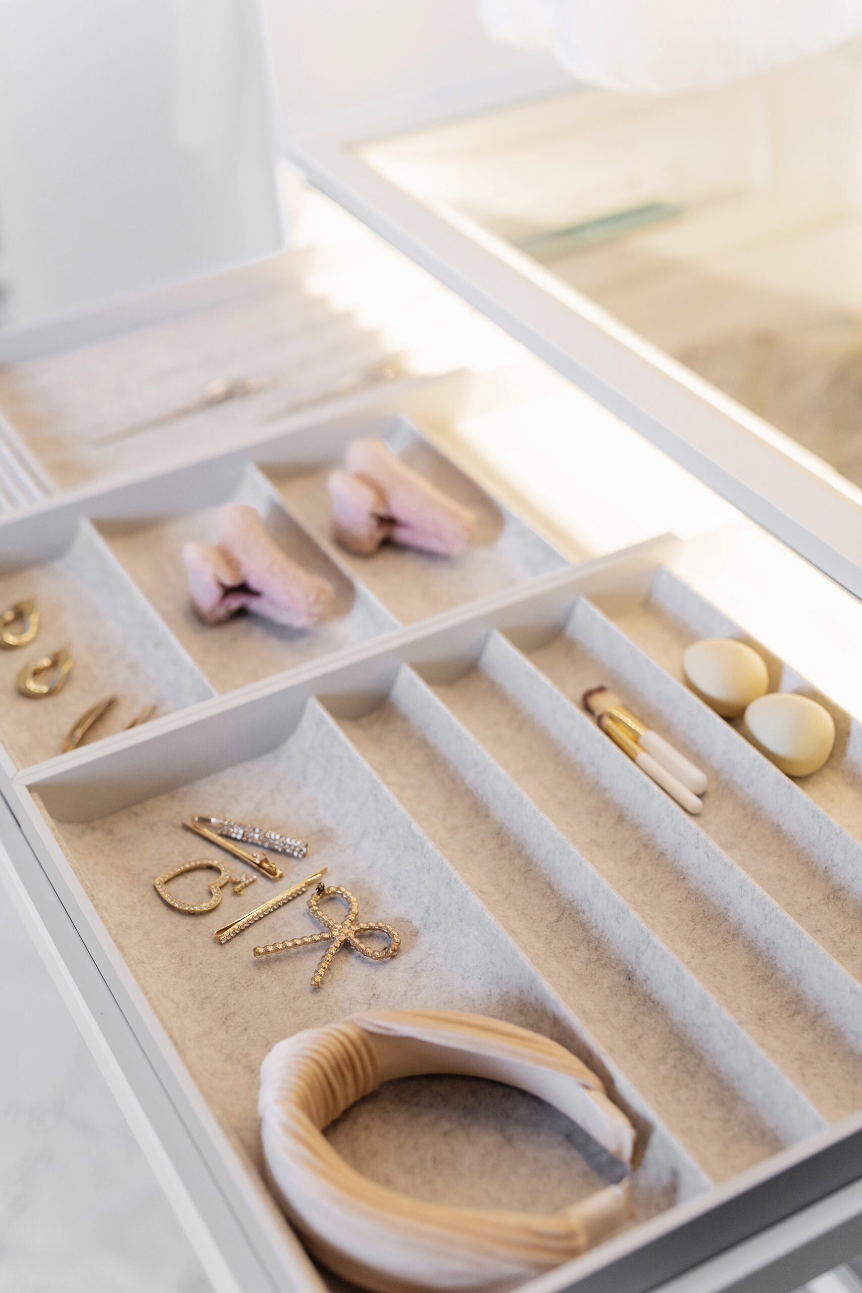 A drawer organizer displaying neatly stored jewelry, including earrings, rings, and bracelets, along with a headband and cotton swabs, all arranged in soft, padded compartments for a luxurious and organized feel.