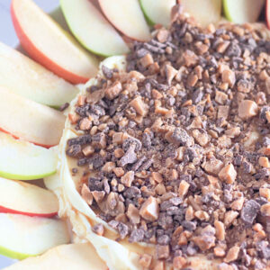A close-up shot showcasing the rich texture of a toffee apple dip, with a layer of smooth cream cheese mixture and a generous topping of crushed toffee pieces.
