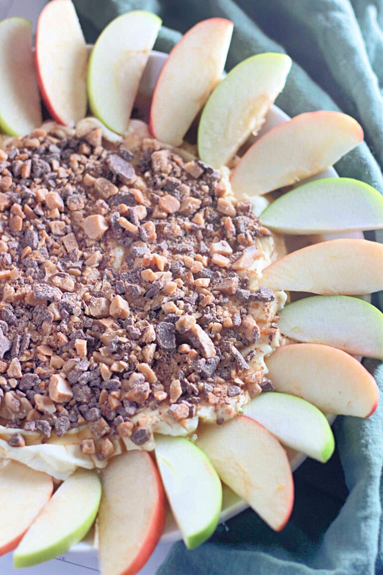 A side angle capturing the contrast between the creamy caramel-infused dip and the crisp apple slices, highlighting the rich, crunchy toffee topping.