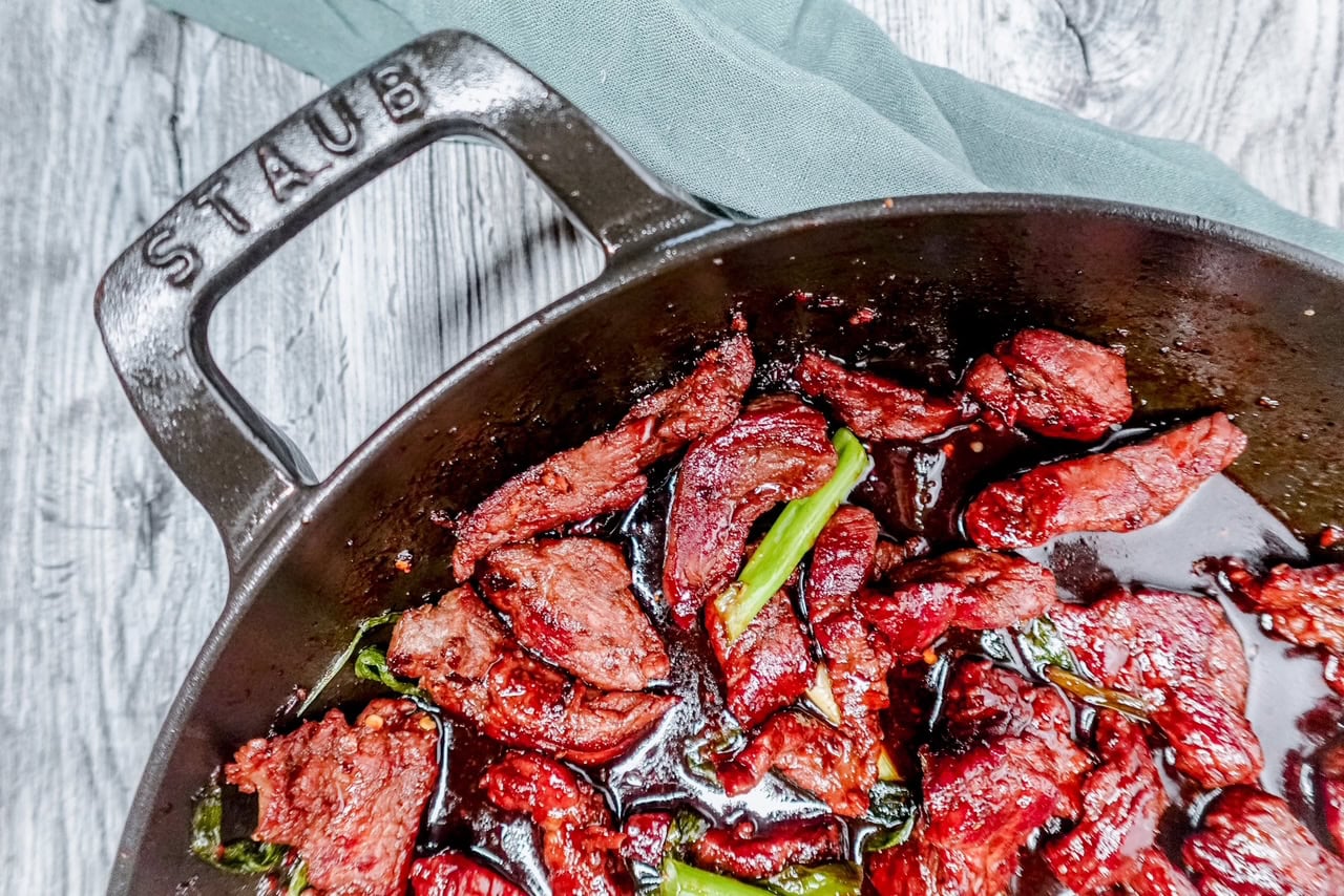 Angled close-up of keto Mongolian beef with vibrant green onion garnishes, nestled in a cast iron skillet, perfect for a low-carb Asian-inspired dinner.