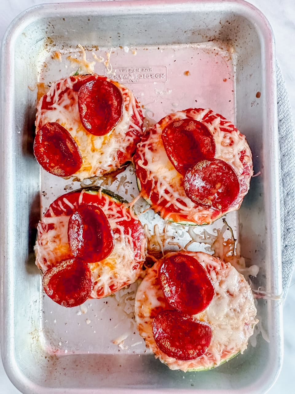 Freshly baked zucchini pepperoni pizzas still in the tray, with melted cheese and crispy edges on the pepperoni.