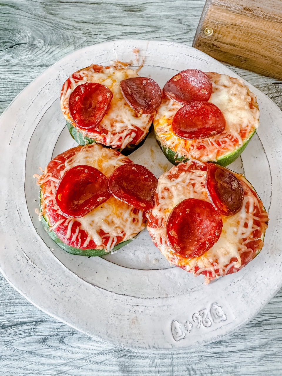 Close-up of cheesy zucchini pizzas on a rustic white plate, showing the crispy pepperoni and gooey melted cheese.