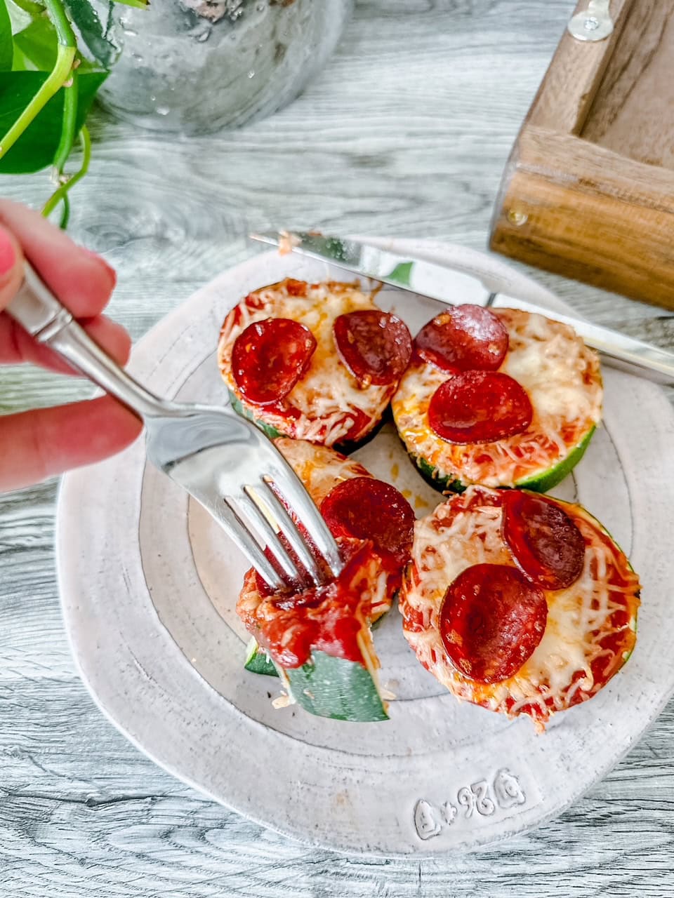 A fork lifting a bite of zucchini pepperoni pizza off a plate, showing the layers of zucchini, tomato sauce, melty cheese, and pepperoni—perfect for a low-carb snack or appetizer.