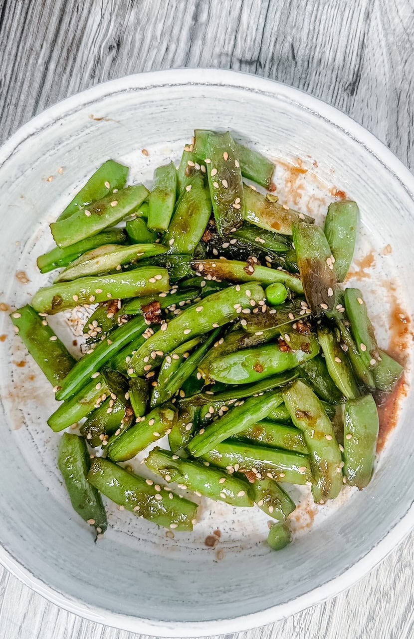 Overhead view of a bowl of glistening sesame snow peas, lightly charred and tossed with a savory sauce and sesame seeds.