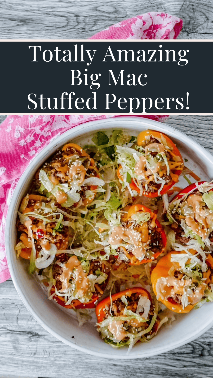 Top-down image of a round white dish filled with colorful Big Mac-inspired stuffed mini peppers, garnished with shredded lettuce, sesame seeds, melted cheese, and creamy sauce, styled on a rustic wooden surface with a pink floral napkin. Overlay text reads “Totally Amazing Big Mac Stuffed Peppers!”