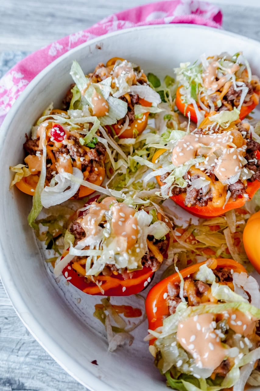 Angled close-up of the Big Mac inspired peppers, highlighting the juicy beef filling, melted cheddar, and tangy sauce with a sprinkle of sesame seeds, set against a white bowl and rustic wood backdrop.
