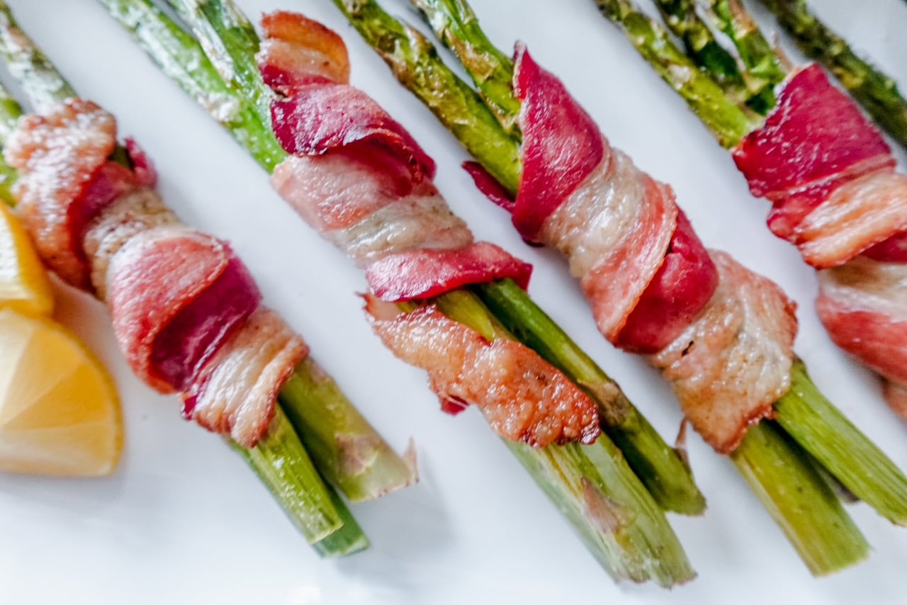 Extreme close-up of crispy bacon-wrapped asparagus bundles highlighting the golden brown bacon edges and juicy asparagus spears.