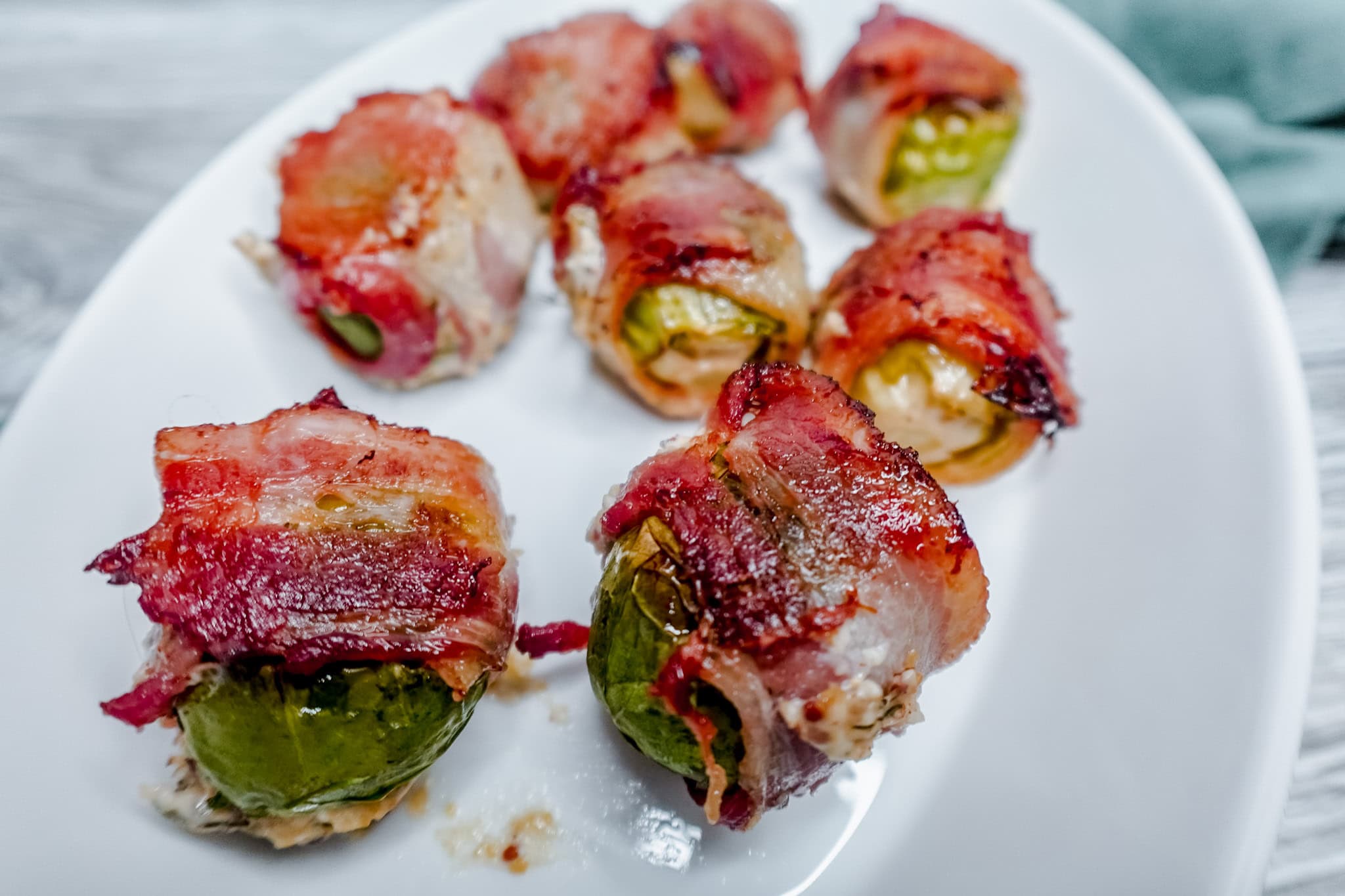 Side angle view of bacon-wrapped Brussels sprouts served on a curved white platter, highlighting their crispy exterior and savory filling.