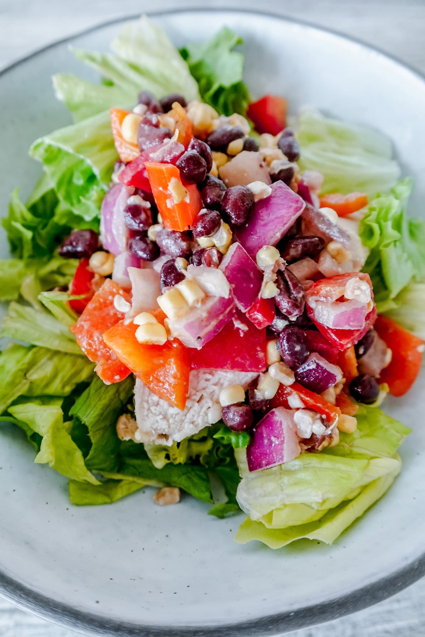 An overhead shot of cowboy caviar chicken salad, highlighting the fresh lettuce base topped with a colorful cowboy caviar mixture of beans, peppers, onions, and corn with chicken.