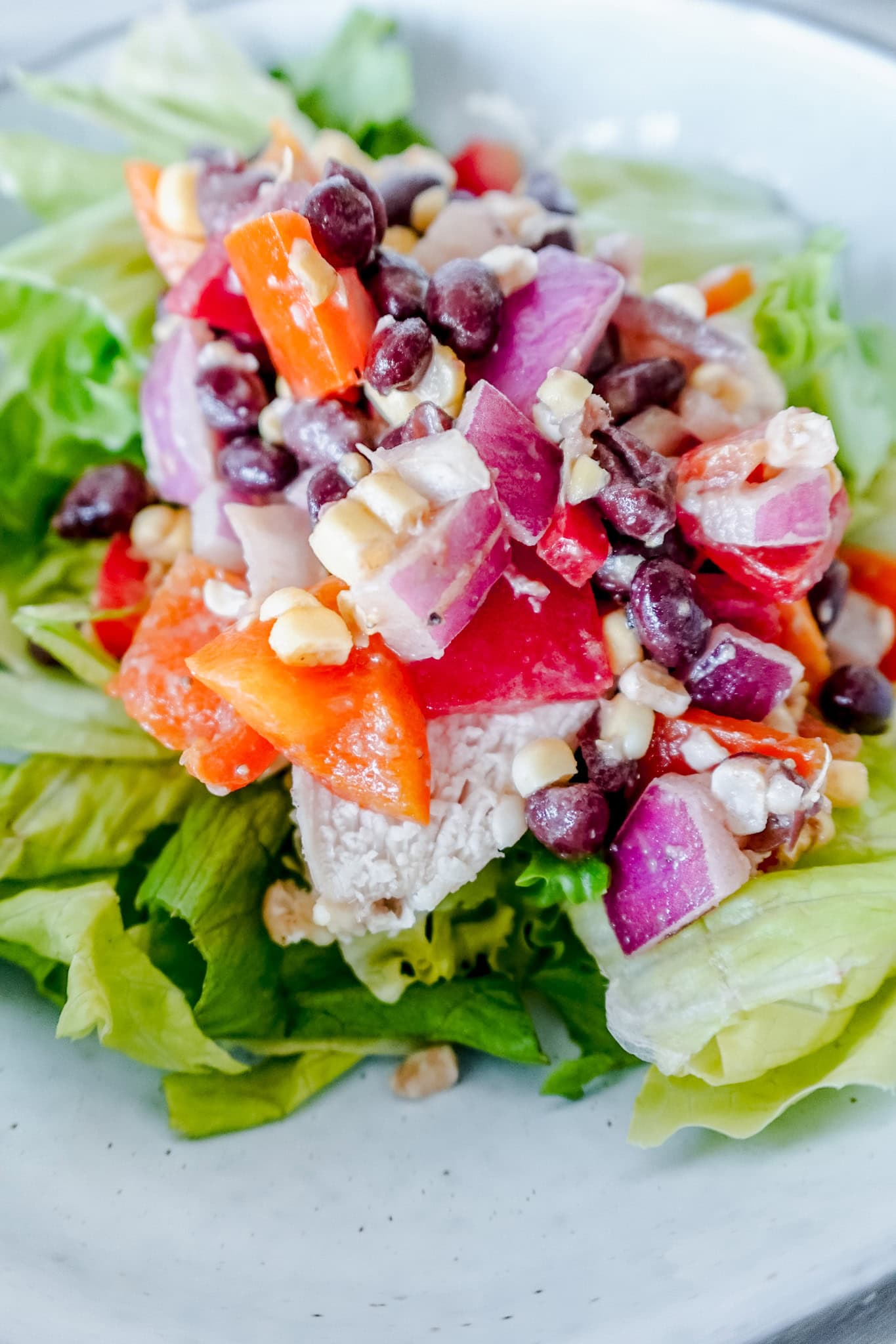 A full bowl of cowboy caviar chicken salad on a wooden background, featuring chopped lettuce, chicken breast, and a vibrant mix of black beans, corn, red onions, and red bell pepper.