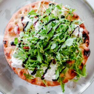 Close-up of the pizza's edge, highlighting the creamy burrata, fresh arugula leaves, and glossy balsamic glaze over a golden crust.