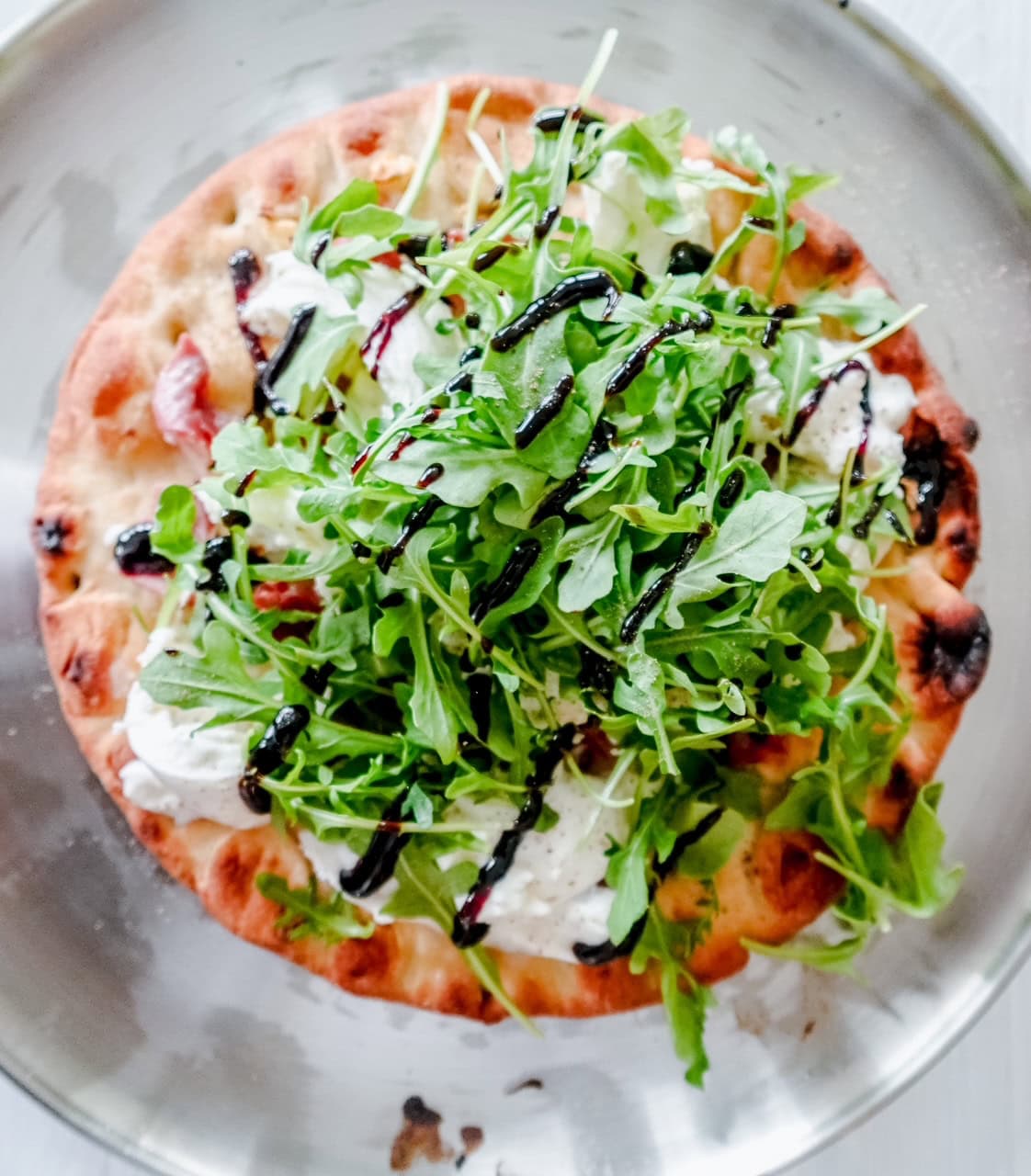 Close-up of the pizza's edge, highlighting the creamy burrata, fresh arugula leaves, and glossy balsamic glaze over a golden crust.