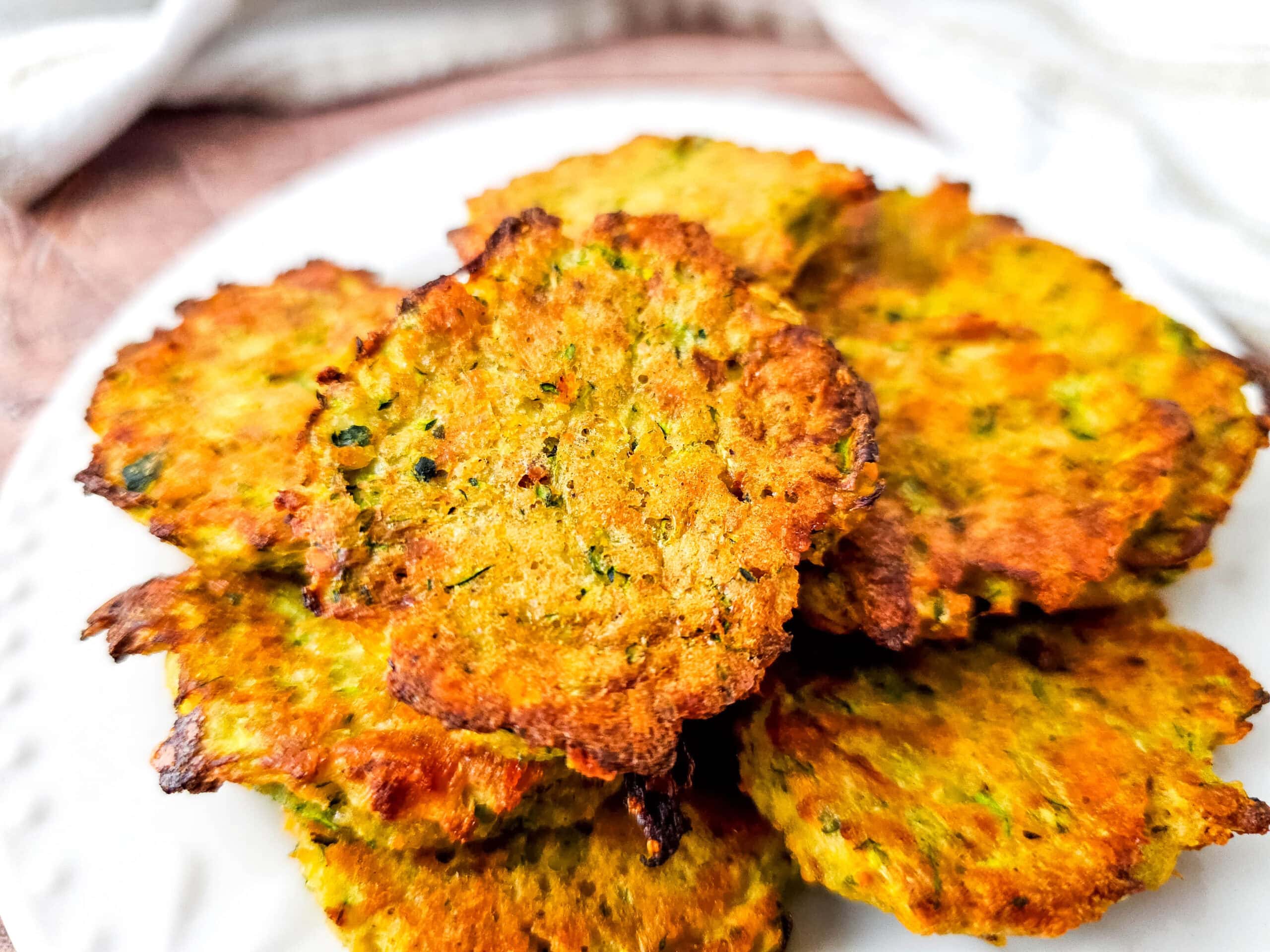 Side angle close-up of crispy zucchini tots piled high on a white plate, showcasing their texture and crispy edges.