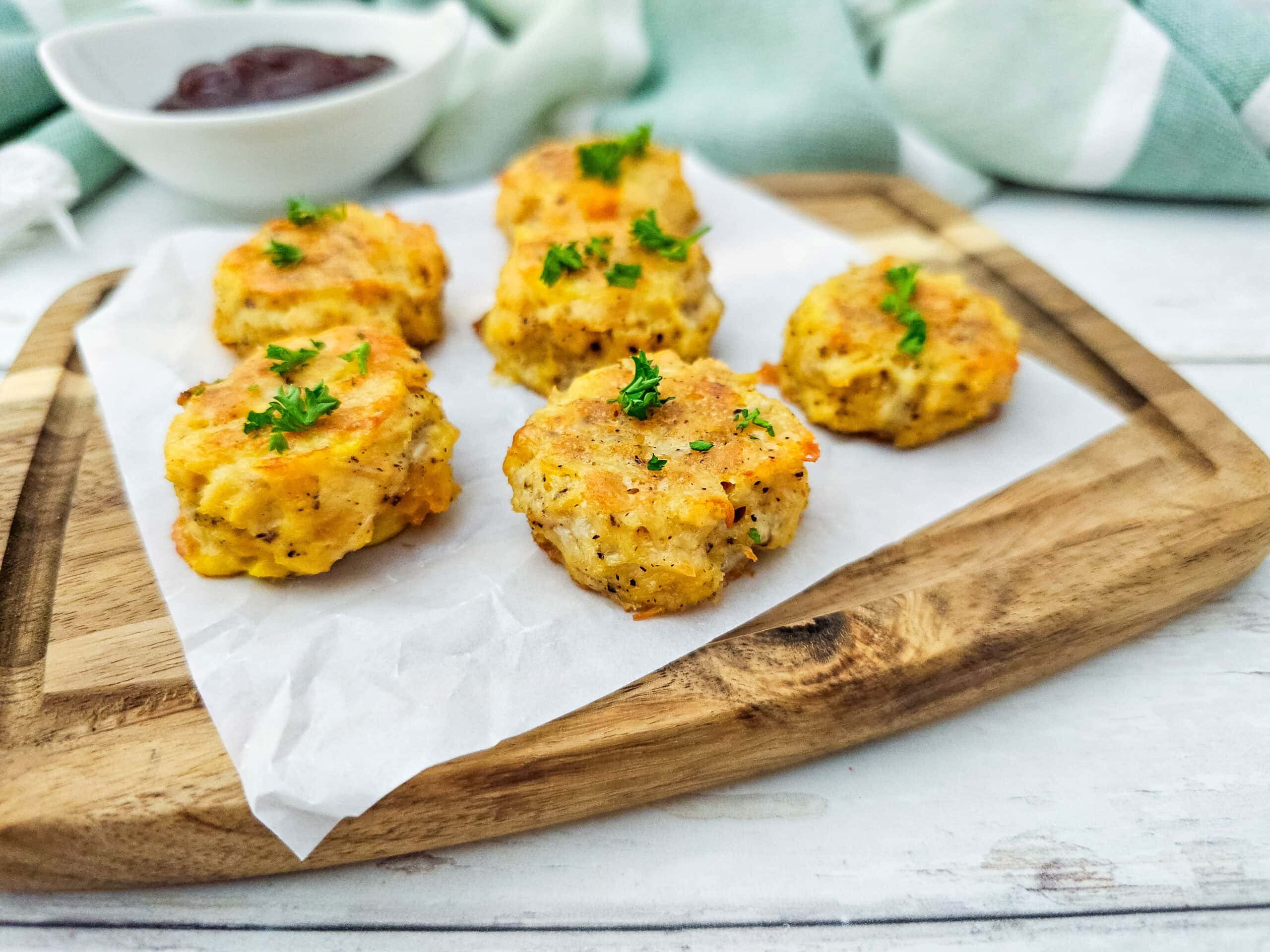 Angled view of low carb chicken nuggets with parsley garnish on parchment paper, showing their golden, cheesy crust.