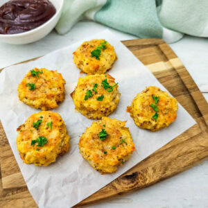 Overhead shot of bite-sized low carb chicken nuggets arranged neatly on a wooden board, served with a small bowl of dipping sauce.